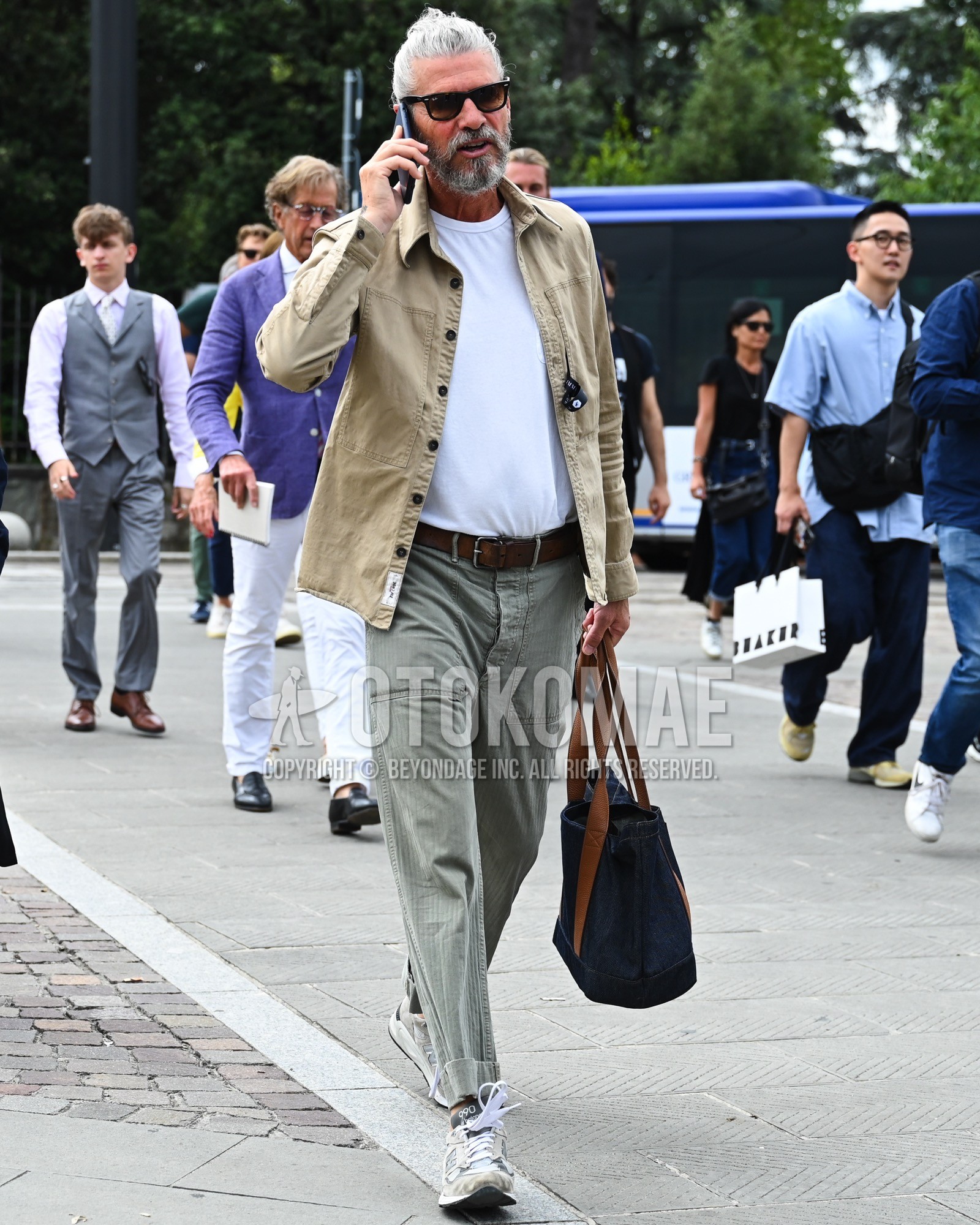 Men's spring summer autumn outfit with brown plain sunglasses, beige plain shirt jacket, white plain t-shirt, brown plain leather belt, gray plain bottoms, white low-cut sneakers, navy plain tote bag.