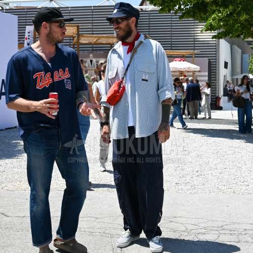 ネイビーワンポイントのキャップ、ブラウンべっ甲のサングラス、レッドストールのバンダナ/ネッカチーフ、グリーンストライプのシャツ、白無地のTシャツ、ネイビー無地のカーゴパンツ、白ローカットのスニーカー、オレンジ無地のサコッシュを合わせた春夏のメンズコーデ・着こなし。