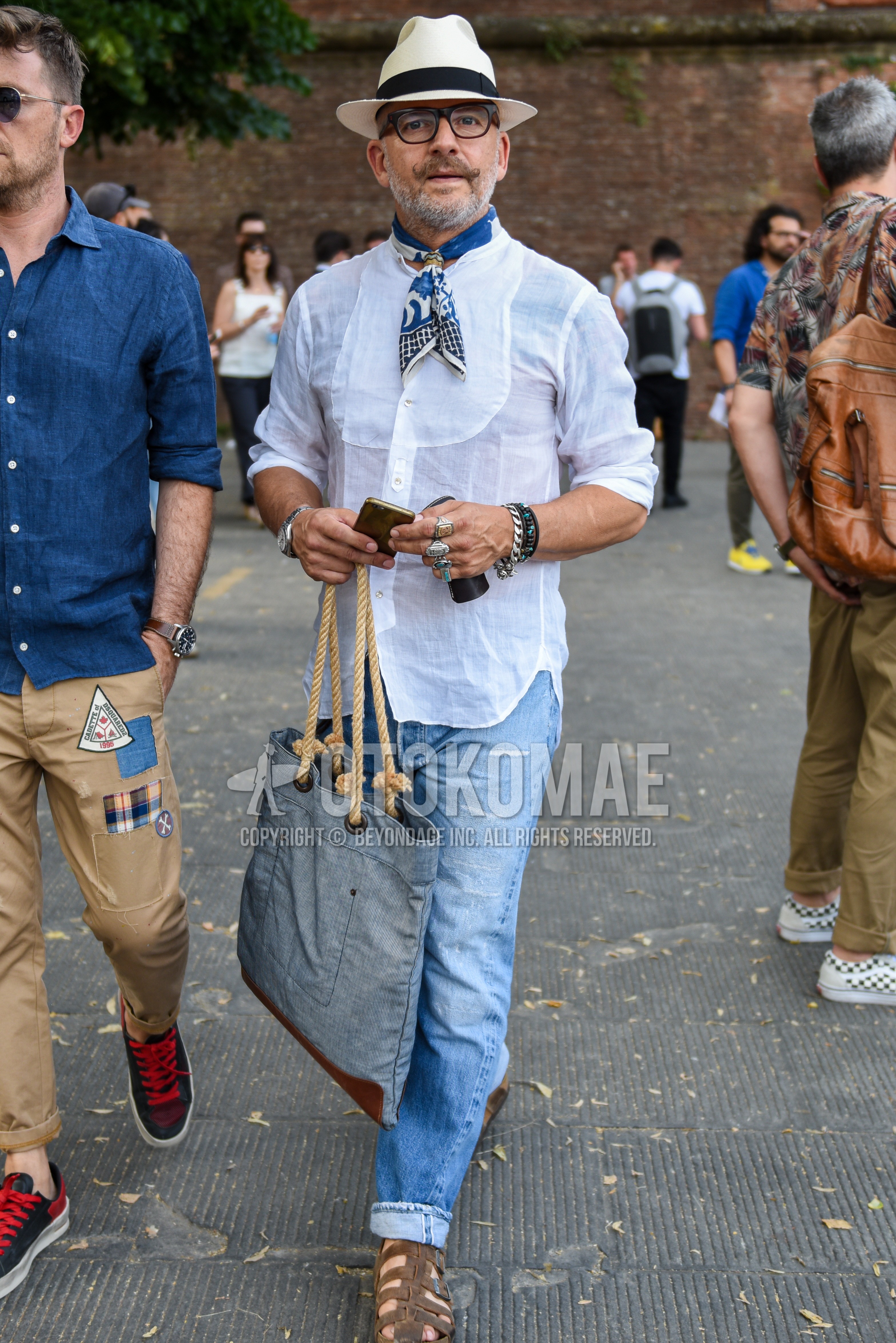 Men's summer outfit with white plain hat, black plain glasses, multi-color plain bandana/neckerchief, white plain shirt, blue plain denim/jeans, brown gurkha sandals, gray plain tote bag.