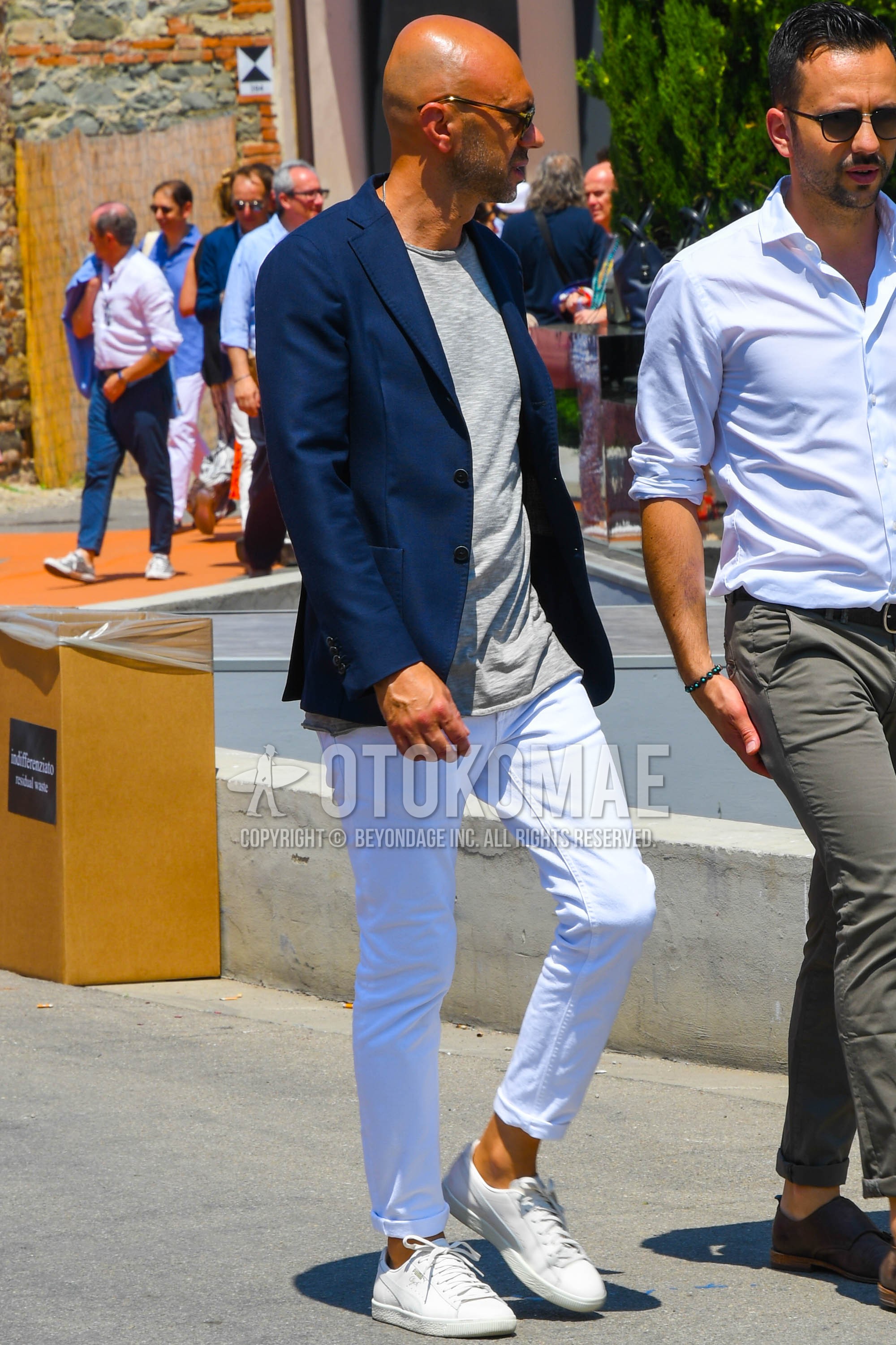 Men's spring summer autumn outfit with navy plain tailored jacket, white plain cotton pants, white low-cut sneakers.