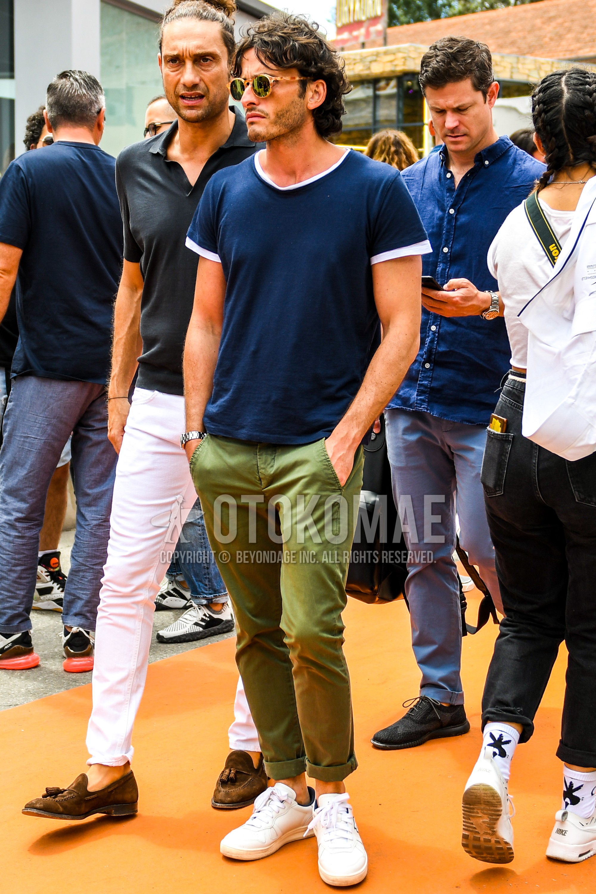 Men's summer outfit with tortoiseshell sunglasses, navy plain t-shirt, white plain t-shirt, olive green plain chinos, white low-cut sneakers.
