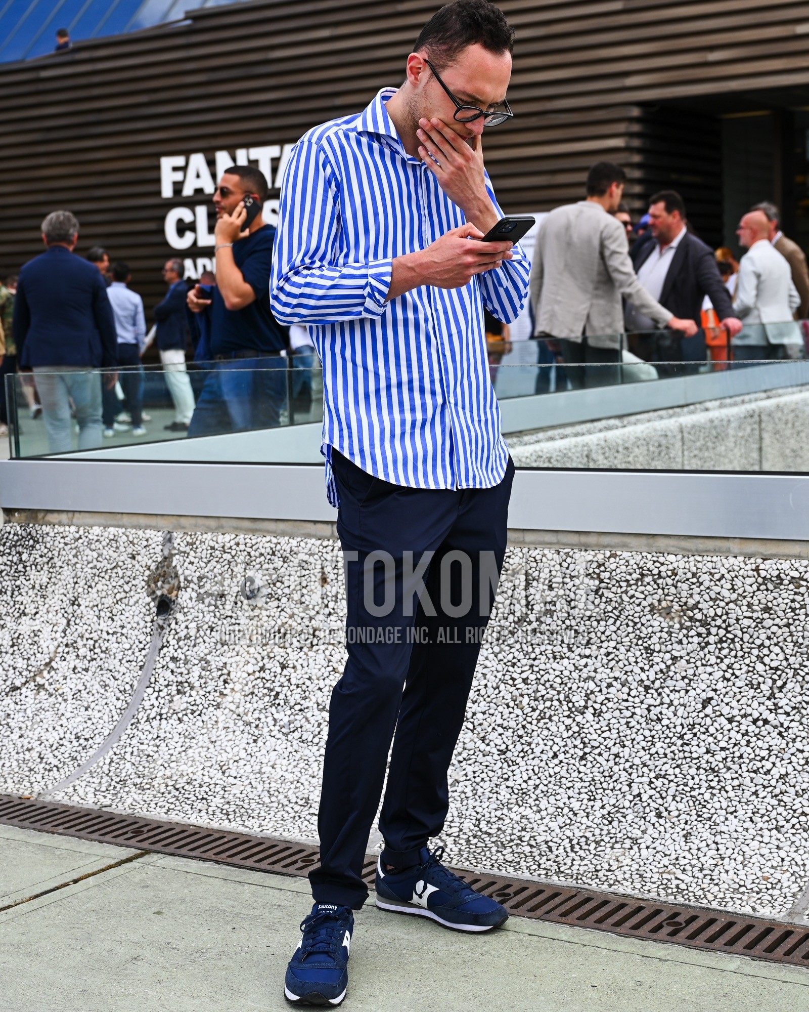 Men's spring summer autumn outfit with clear plain sunglasses, blue stripes shirt, navy plain chinos, navy low-cut sneakers.
