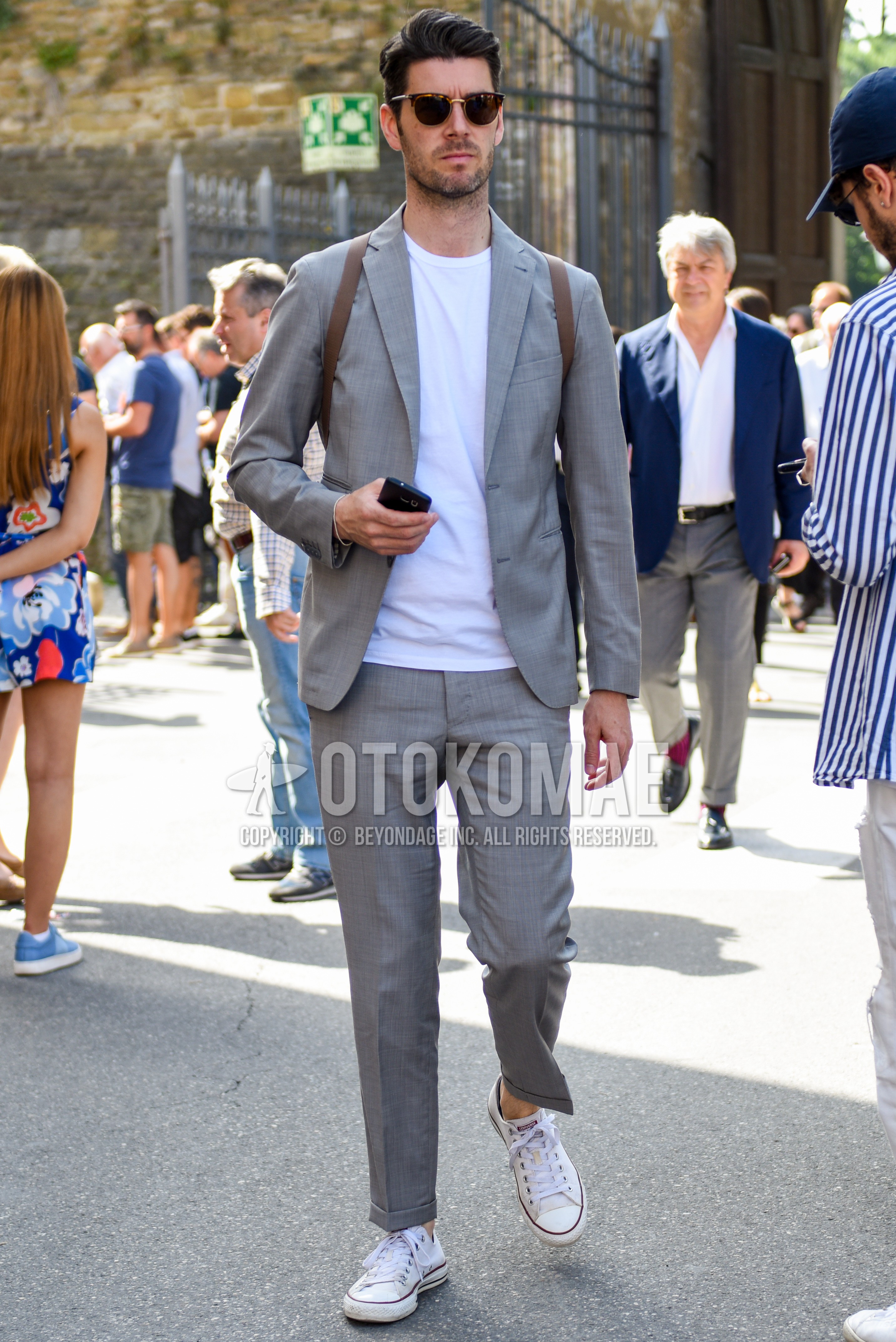 Men's spring summer autumn outfit with brown tortoiseshell sunglasses, white plain t-shirt, white low-cut sneakers, gray plain suit.
