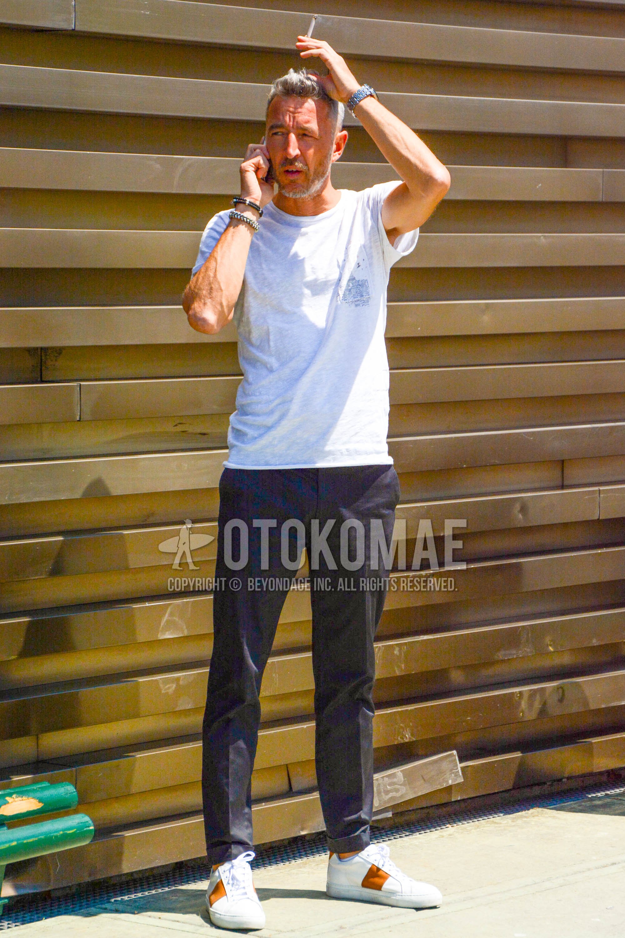 Men's spring summer outfit with white graphic t-shirt, dark gray plain slacks, white low-cut sneakers.