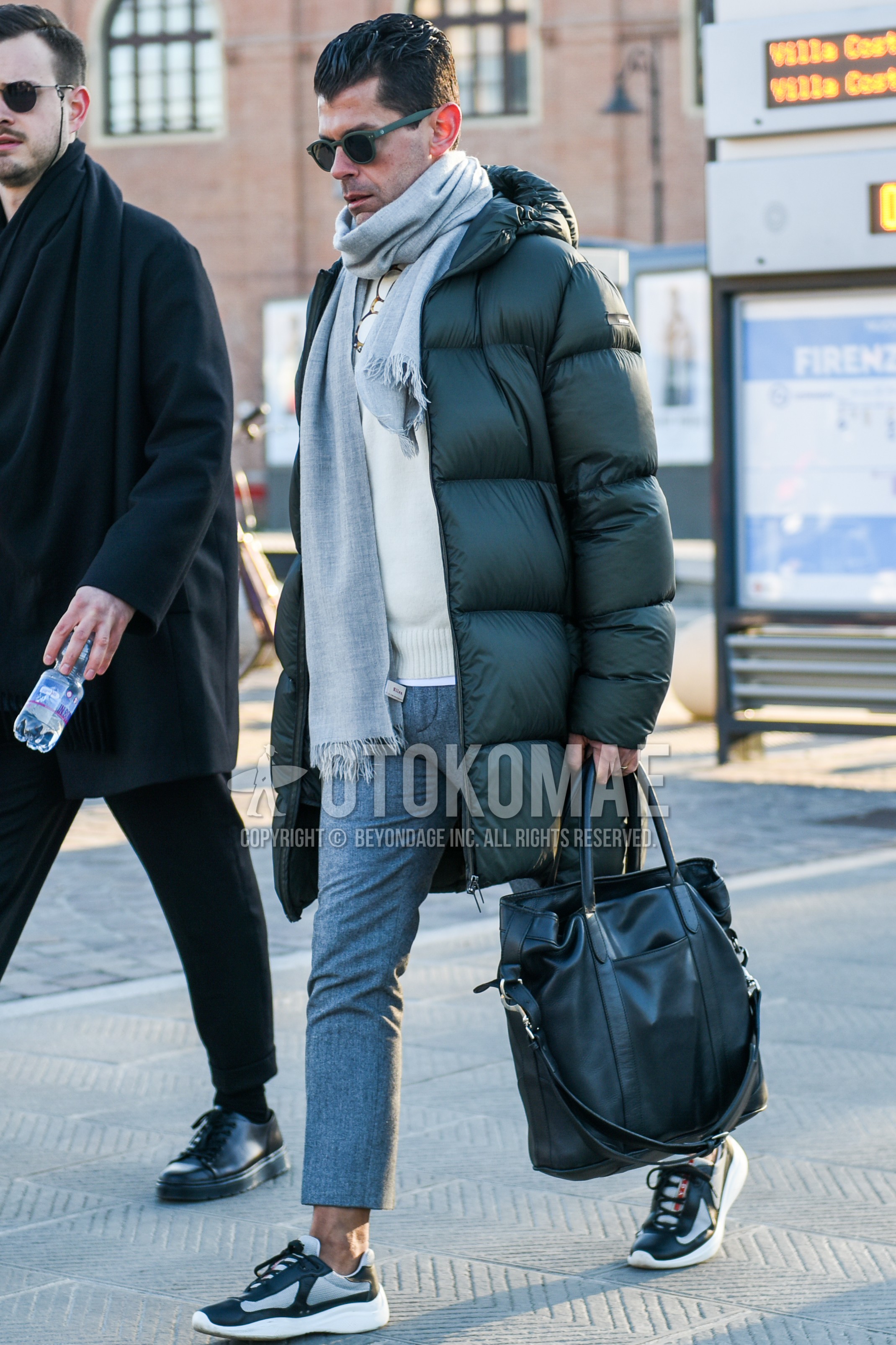 Men's autumn winter outfit with gray plain sunglasses, gray plain scarf, gray plain down jacket, gray plain hooded coat, white graphic sweater, gray plain slacks, gray plain cropped pants, gray low-cut sneakers, black plain briefcase/handbag.