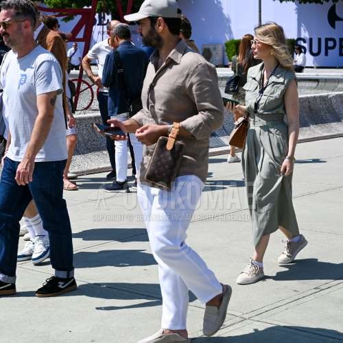 グレー無地のベースボールキャップ、グレー無地のシャツ、白無地のスラックス、白スリッポンのスニーカー、ルイ・ヴィトン　レザーのブラウン小紋のクラッチバッグ/セカンドバッグ/巾着を合わせた春夏のメンズコーデ・着こなし。