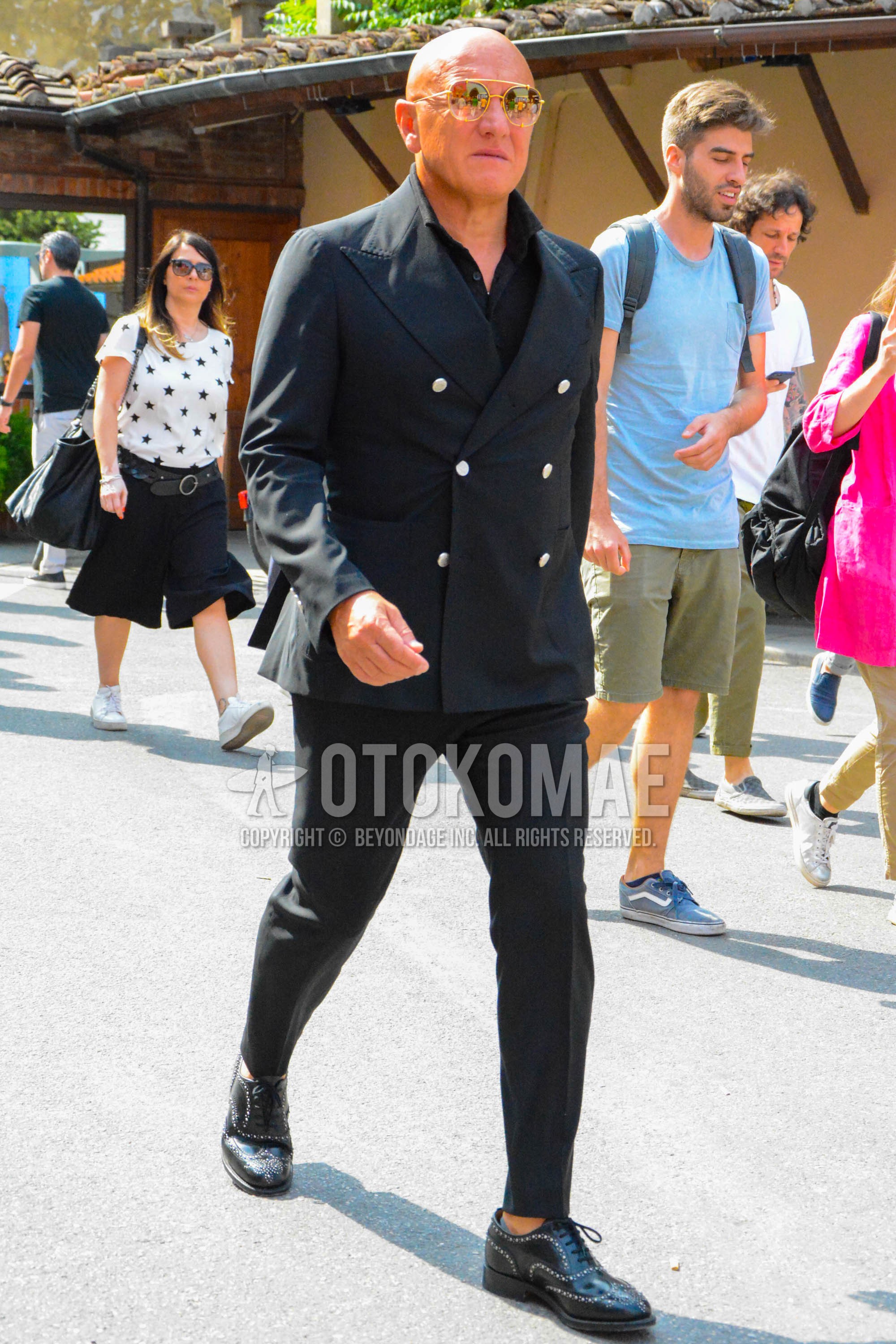 Men's spring summer autumn outfit with gold plain sunglasses, black plain tailored jacket, black plain shirt, black plain slacks, black wing-tip shoes leather shoes.