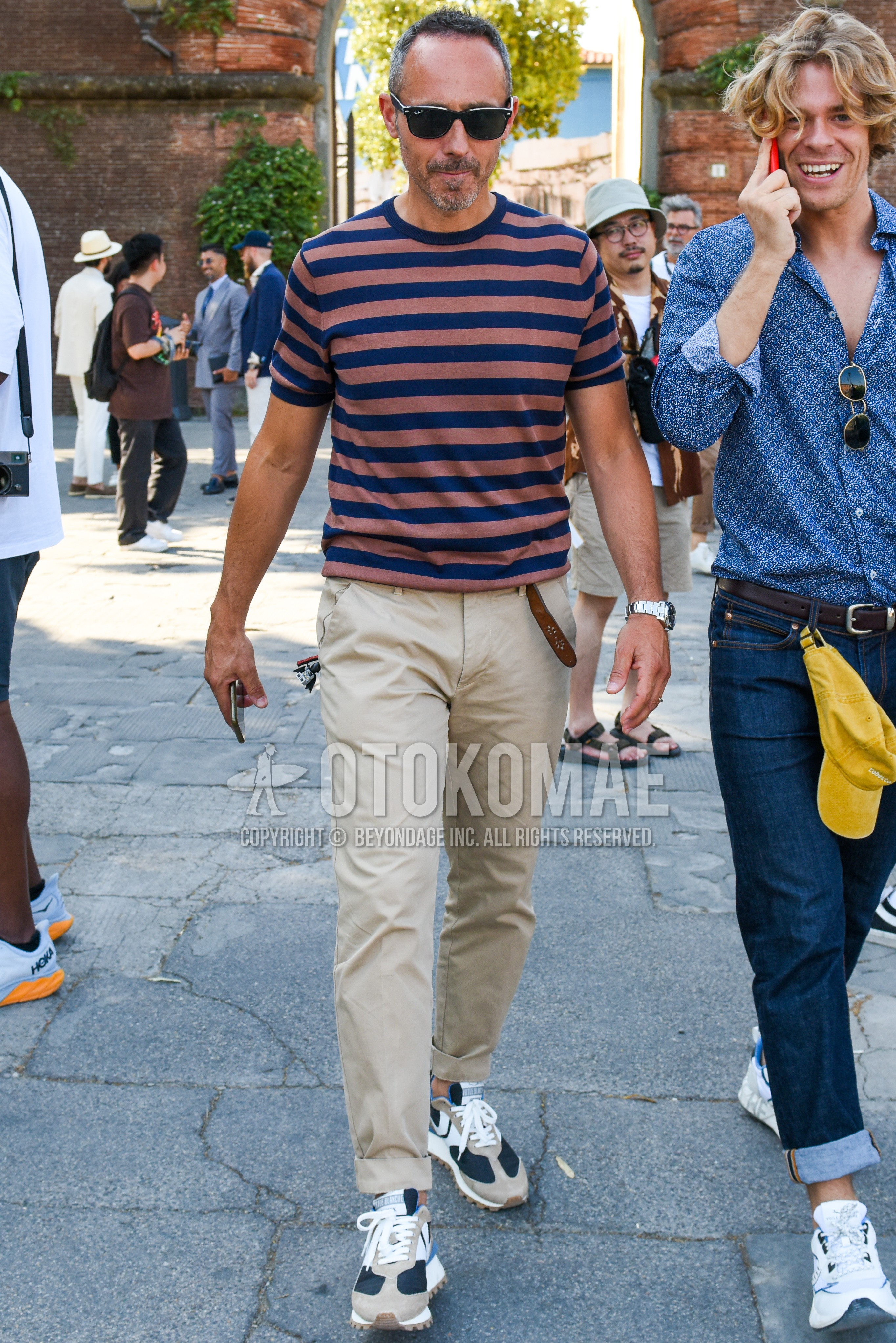 Men's spring summer outfit with navy brown horizontal stripes t-shirt, brown plain leather belt, beige plain chinos, gray navy low-cut sneakers.