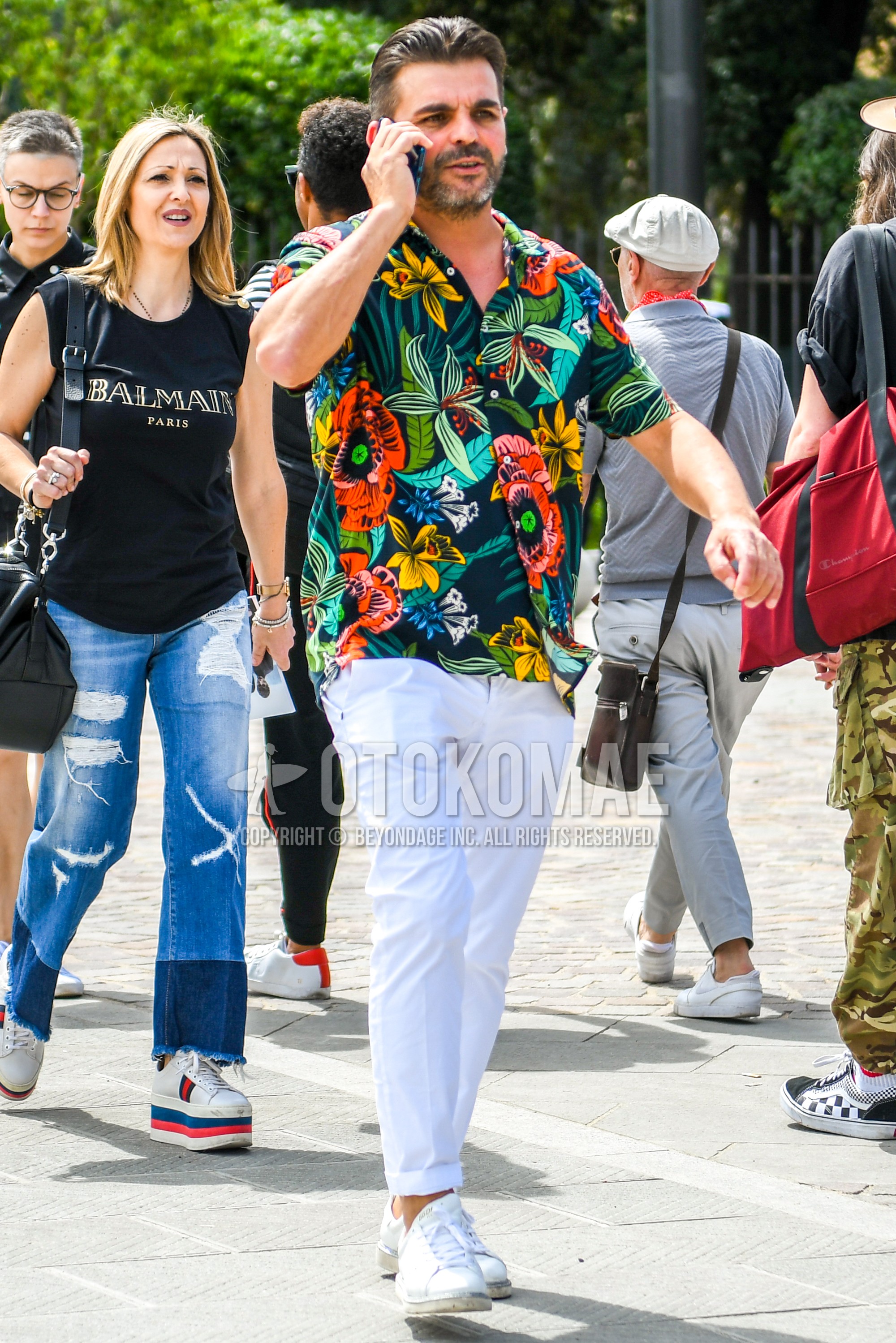 Men's summer outfit with multi-color botanical shirt, white plain ankle pants, white low-cut sneakers.
