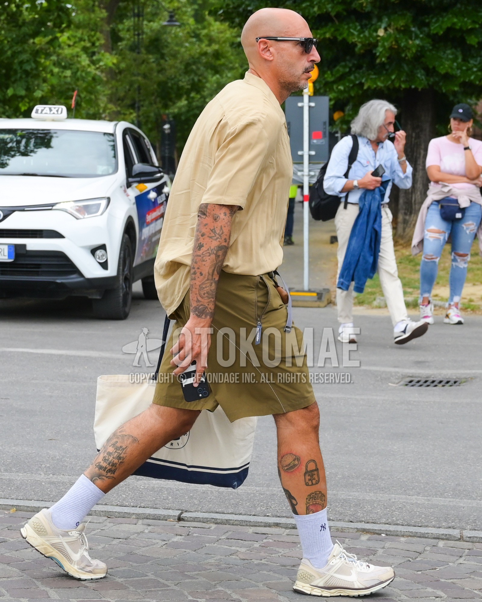 Men's spring summer outfit with black plain sunglasses, beige plain t-shirt, olive green plain short pants, white one point socks, white low-cut sneakers, white one point tote bag.