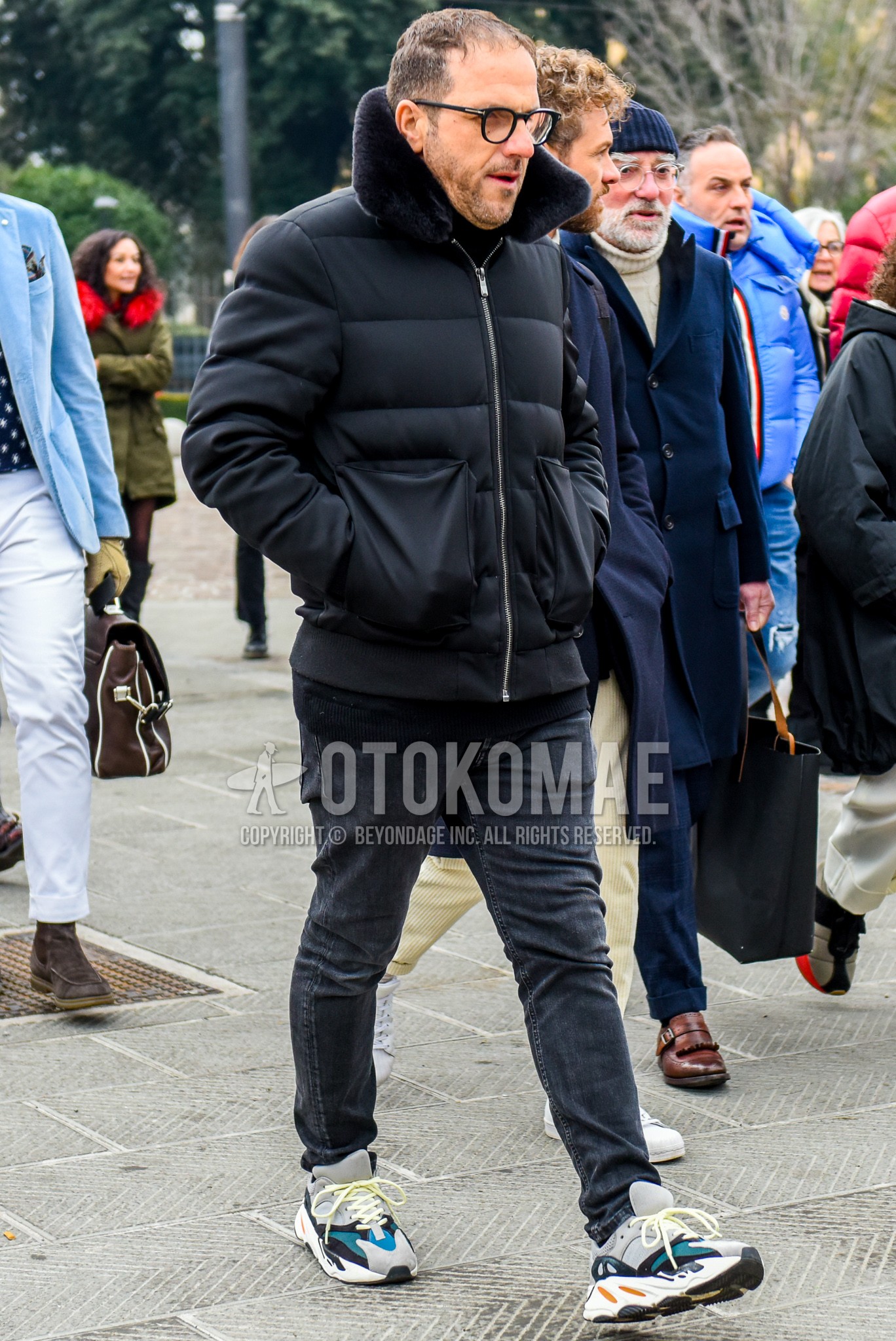 Men's winter outfit with plain glasses, black plain down jacket, dark gray plain denim/jeans, white low-cut sneakers.