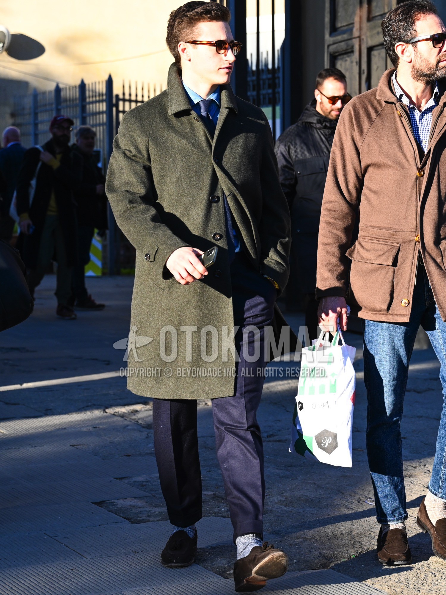 Men's autumn winter outfit with brown plain sunglasses, olive green plain stenkarrer coat, blue plain shirt, navy plain slacks, gray plain socks, brown tassel loafers leather shoes.
