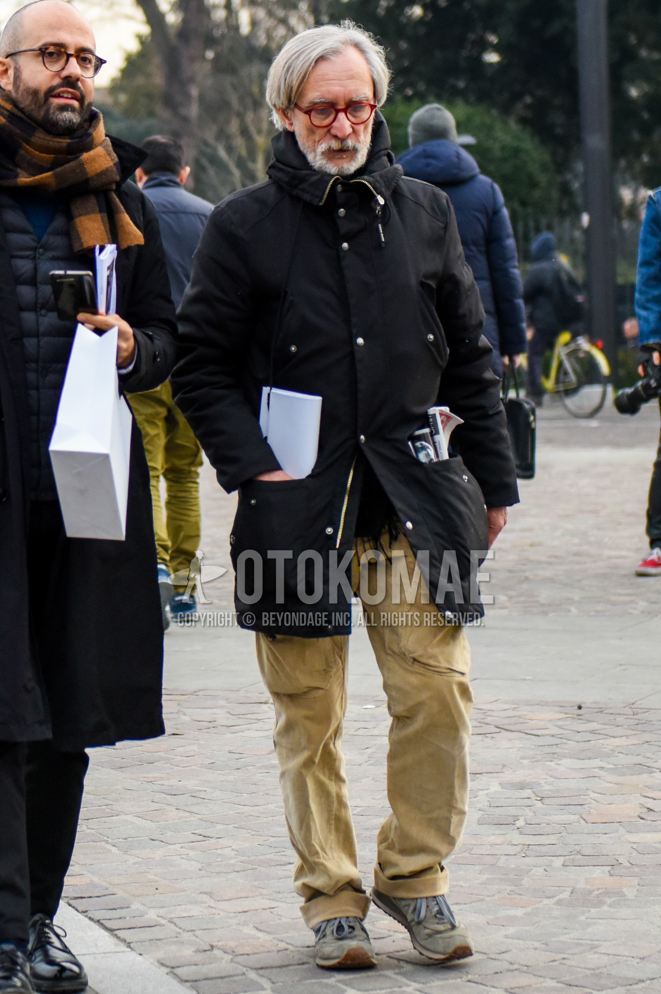 Men's winter outfit with plain glasses, black plain hooded coat, beige plain wide pants, beige low-cut sneakers.