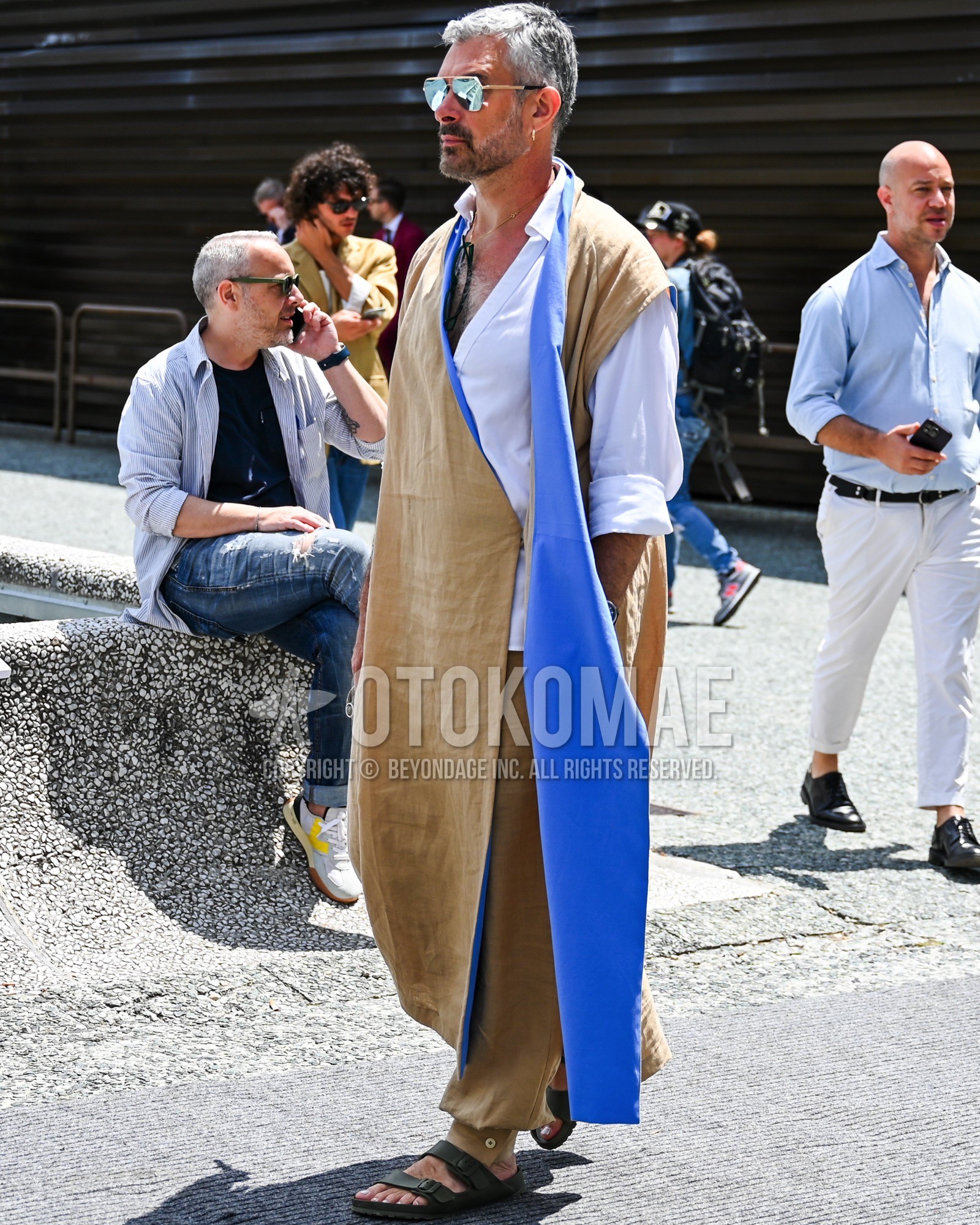 Men's spring summer outfit with silver plain sunglasses, beige plain outerwear, white plain shirt, black sport sandals.