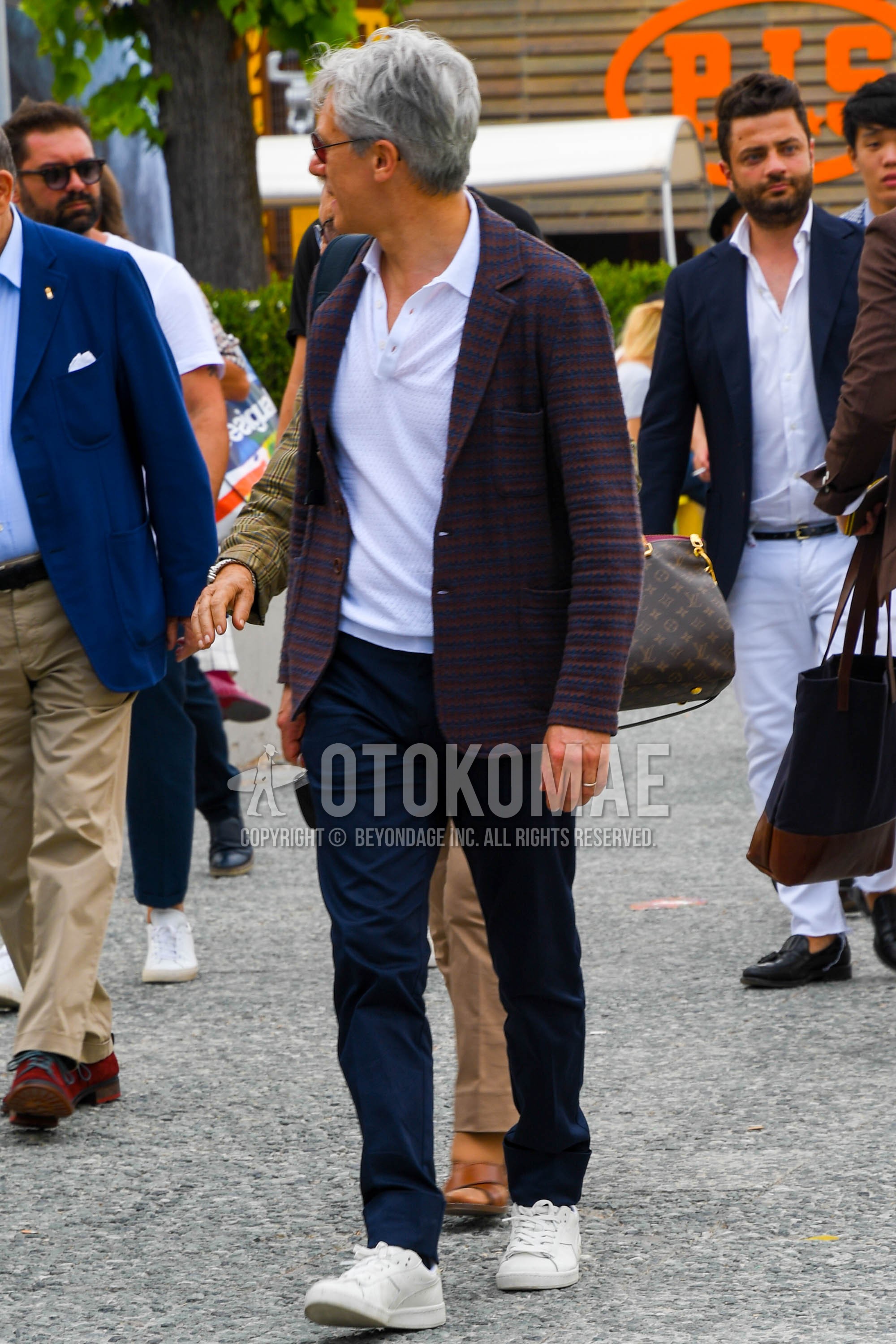 Men's spring summer autumn outfit with brown navy check tailored jacket, white plain polo shirt, navy plain chinos, white low-cut sneakers.