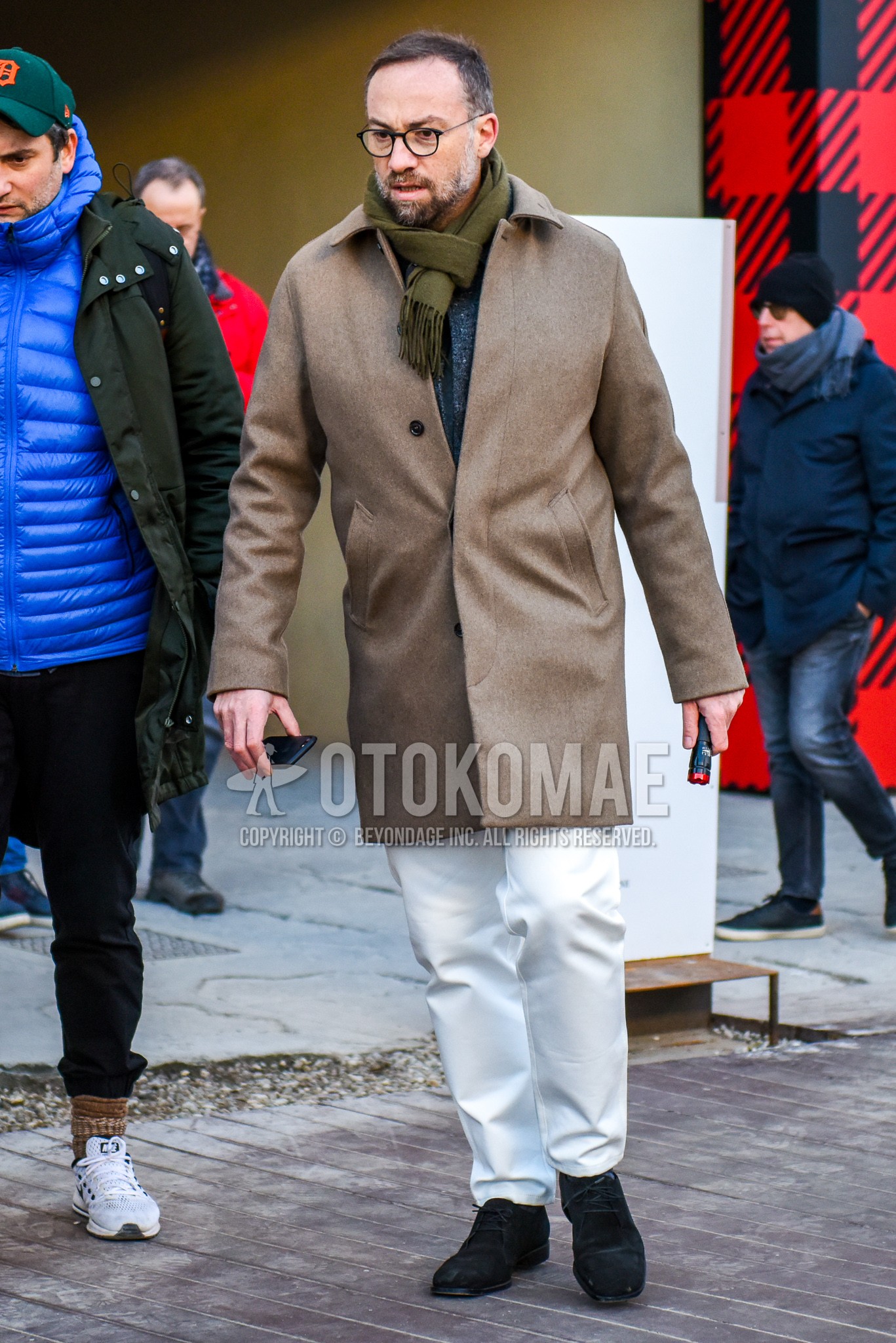 Men's autumn winter outfit with black plain glasses, olive green plain scarf, beige plain stenkarrer coat, white plain cotton pants, black chukka boots.