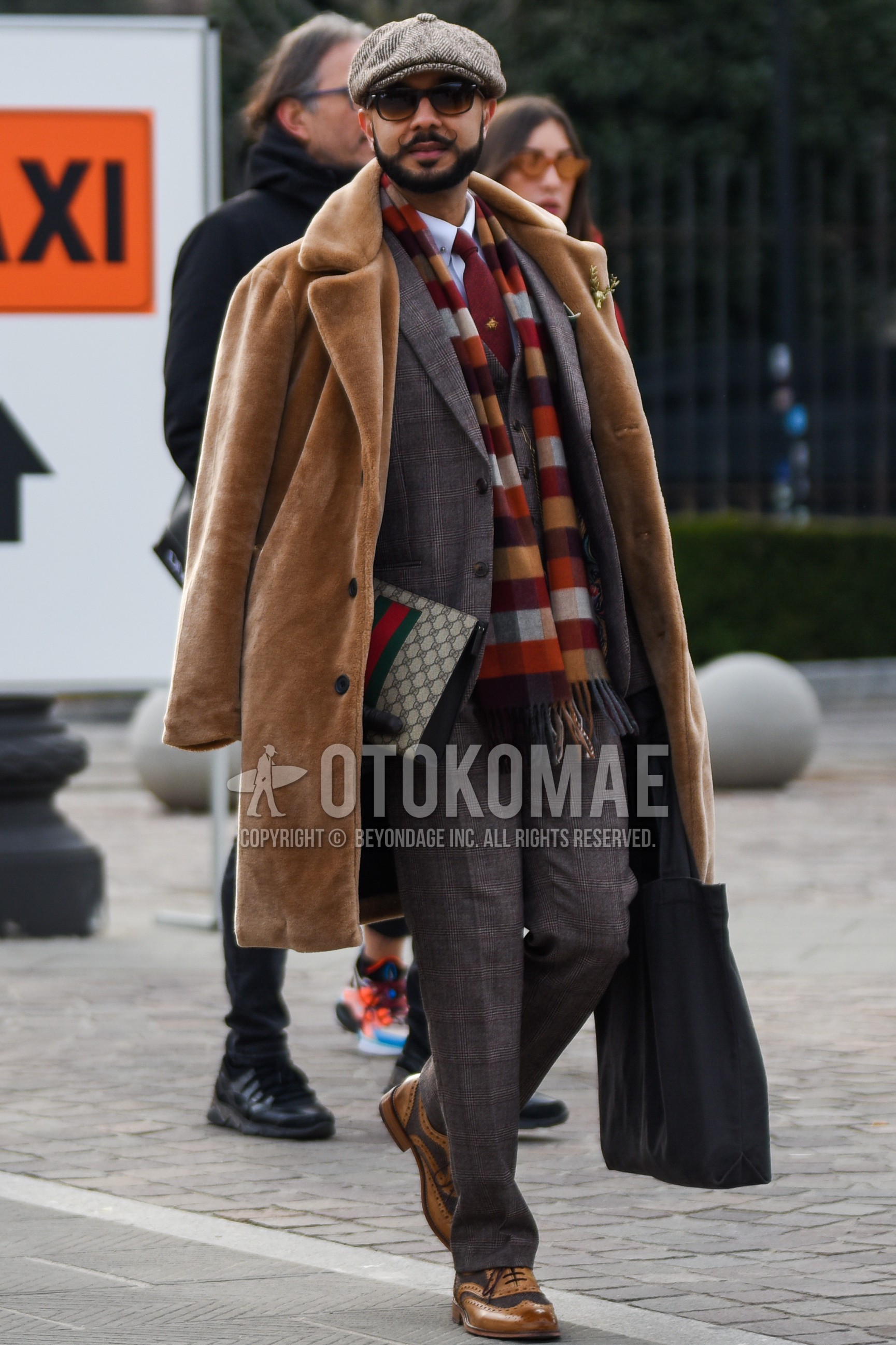 Men's winter outfit with gray herringbone hunting cap, brown plain sunglasses, multi-color check scarf, brown plain chester coat, white plain shirt, brown wing-tip shoes leather shoes, beige bag clutch bag/second bag/drawstring bag, gray check three-piece suit, red one point necktie.