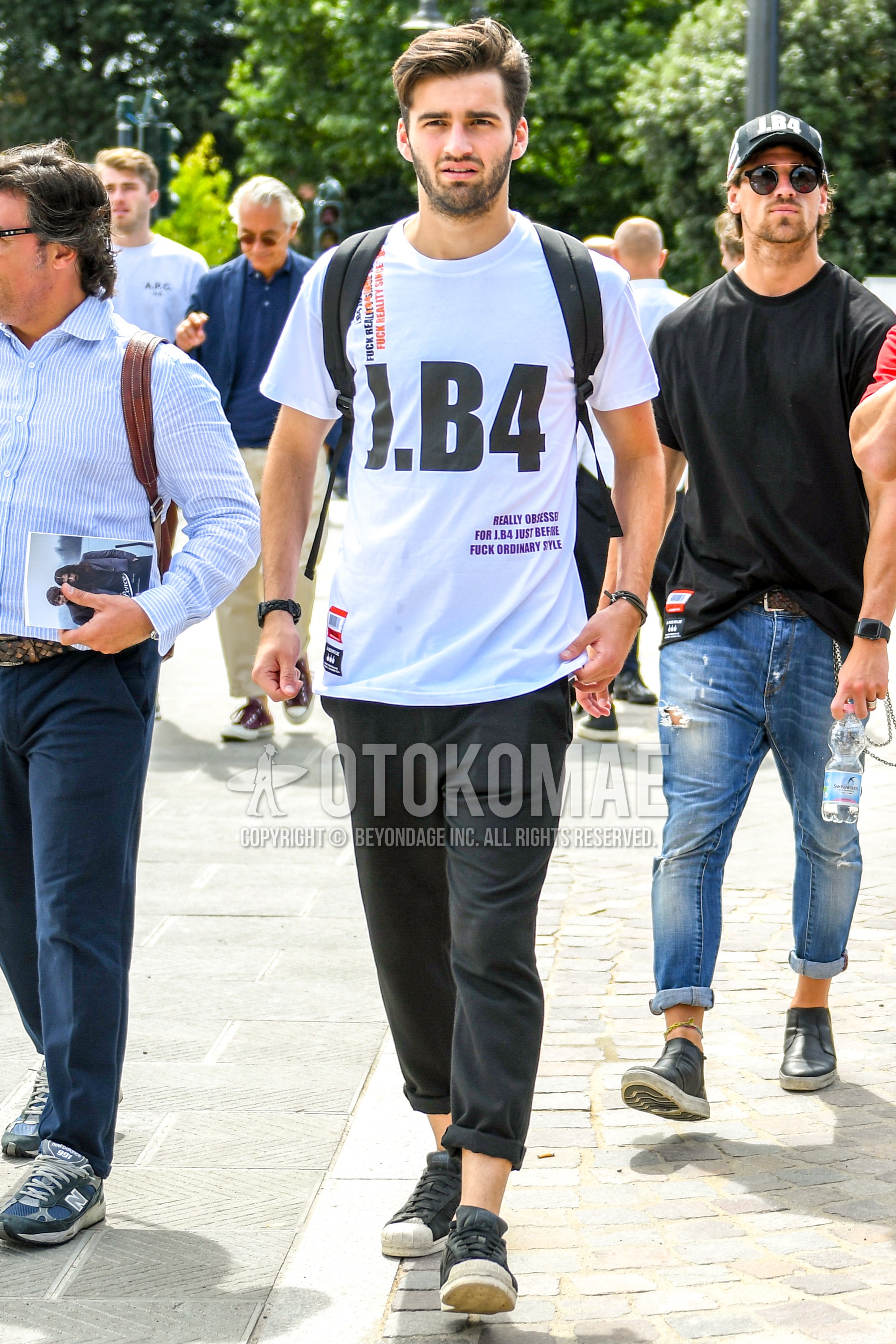 Men's summer outfit with white graphic t-shirt, black plain ankle pants, black low-cut sneakers.