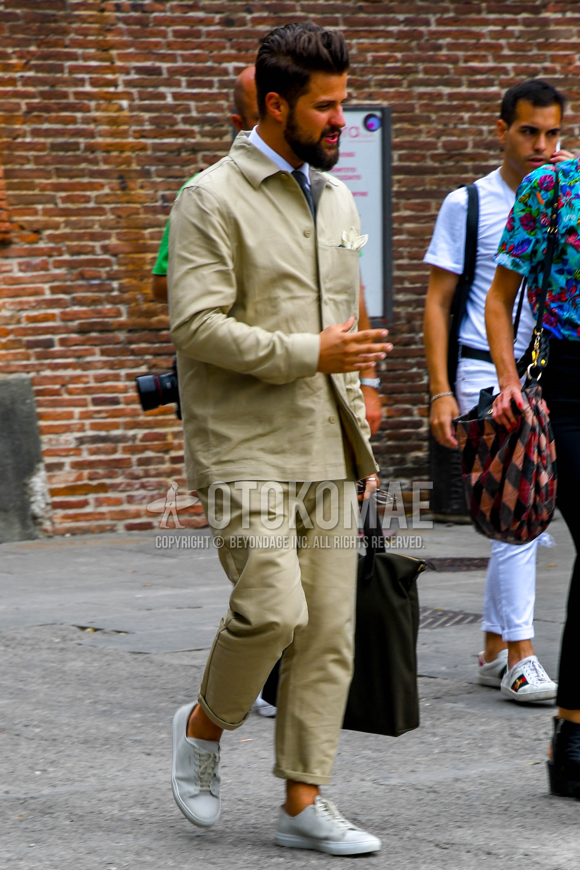 Men's spring autumn outfit with beige plain shirt jacket, white plain shirt, beige plain chinos, white low-cut sneakers.