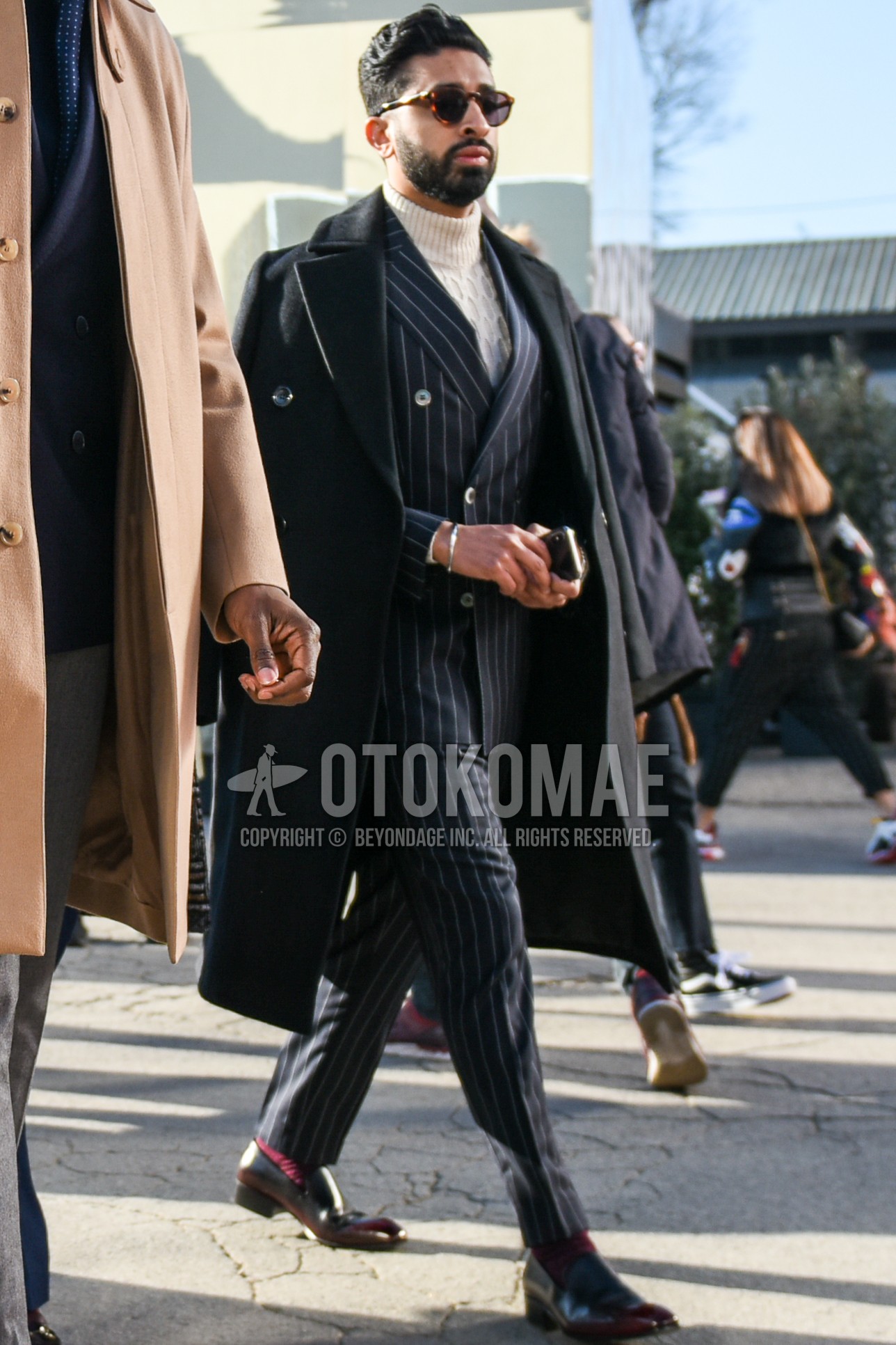 Men's autumn winter outfit with brown tortoiseshell sunglasses, black plain ulster coat, white plain turtleneck knit, red plain socks, brown  loafers leather shoes, gray stripes suit.