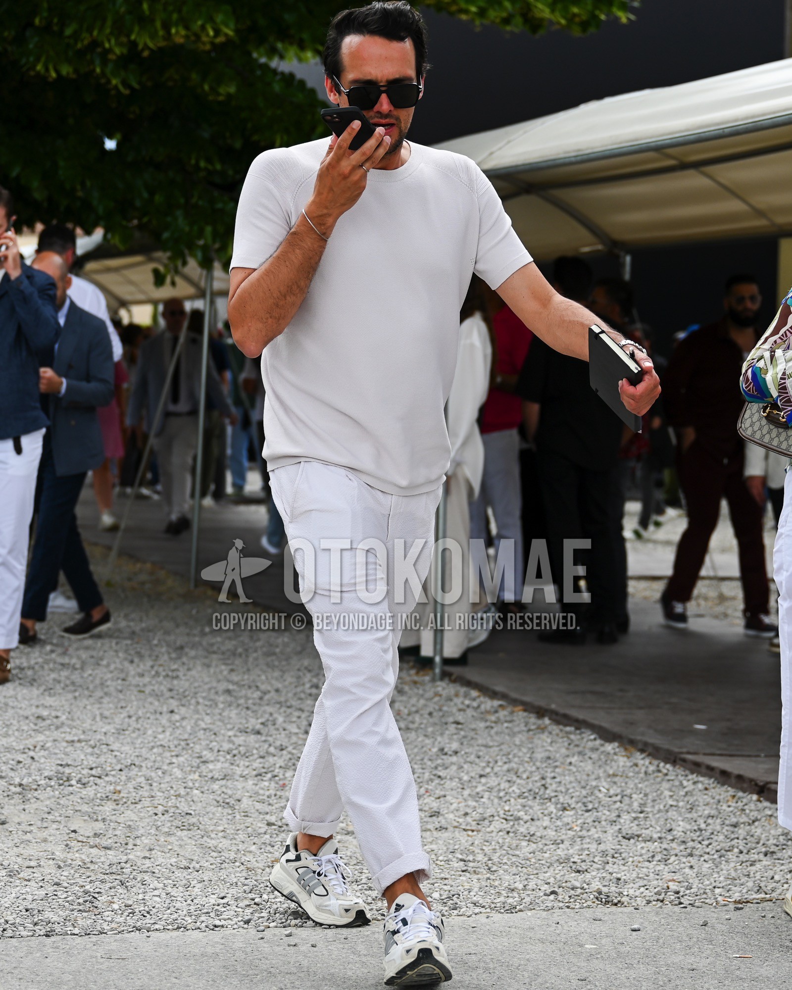 Men's spring summer outfit with black plain sunglasses, white plain t-shirt, white plain chinos, white low-cut sneakers.