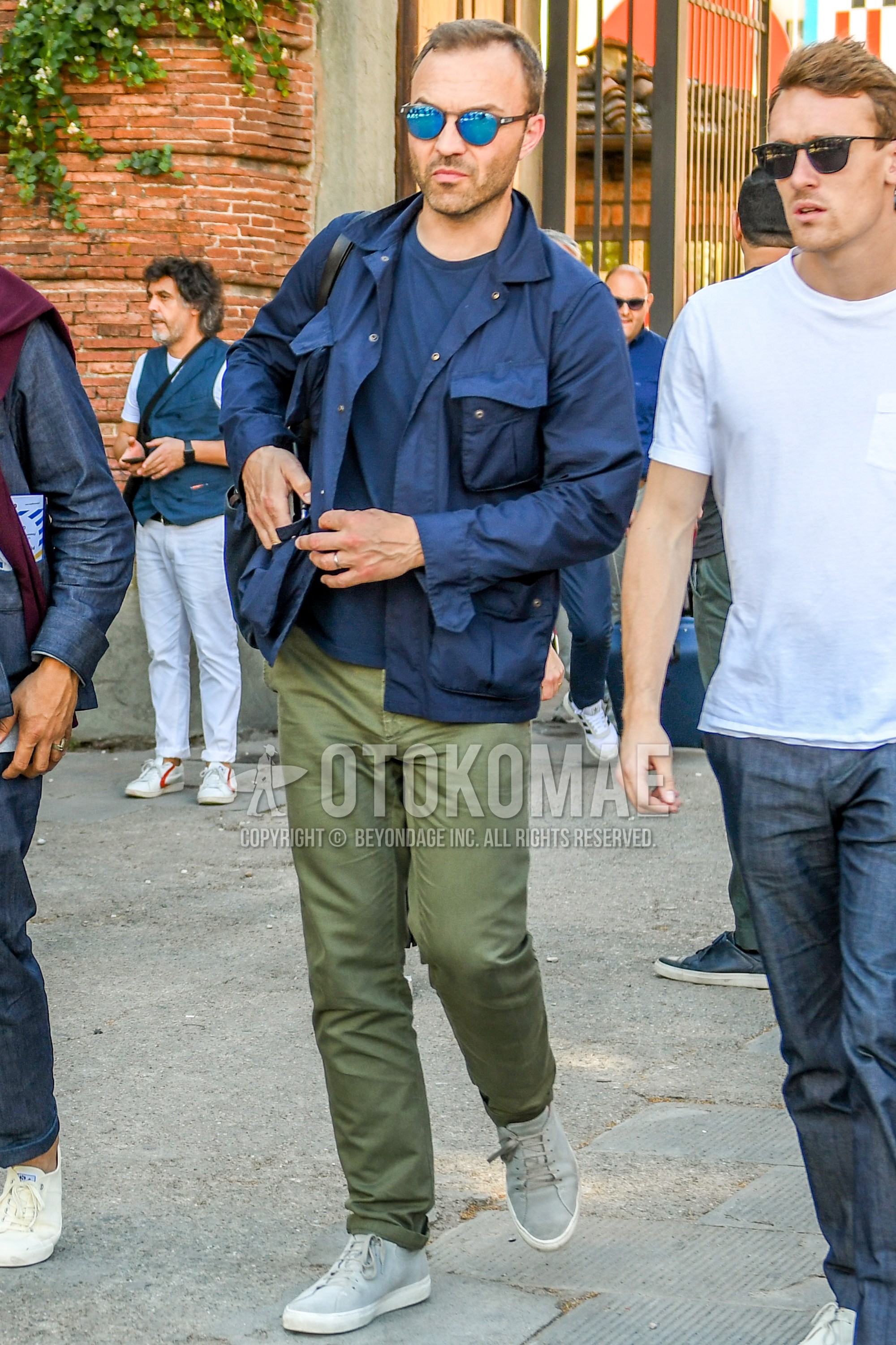 Men's spring summer autumn outfit with plain sunglasses, navy plain M-65, navy plain t-shirt, olive green plain chinos, gray low-cut sneakers.