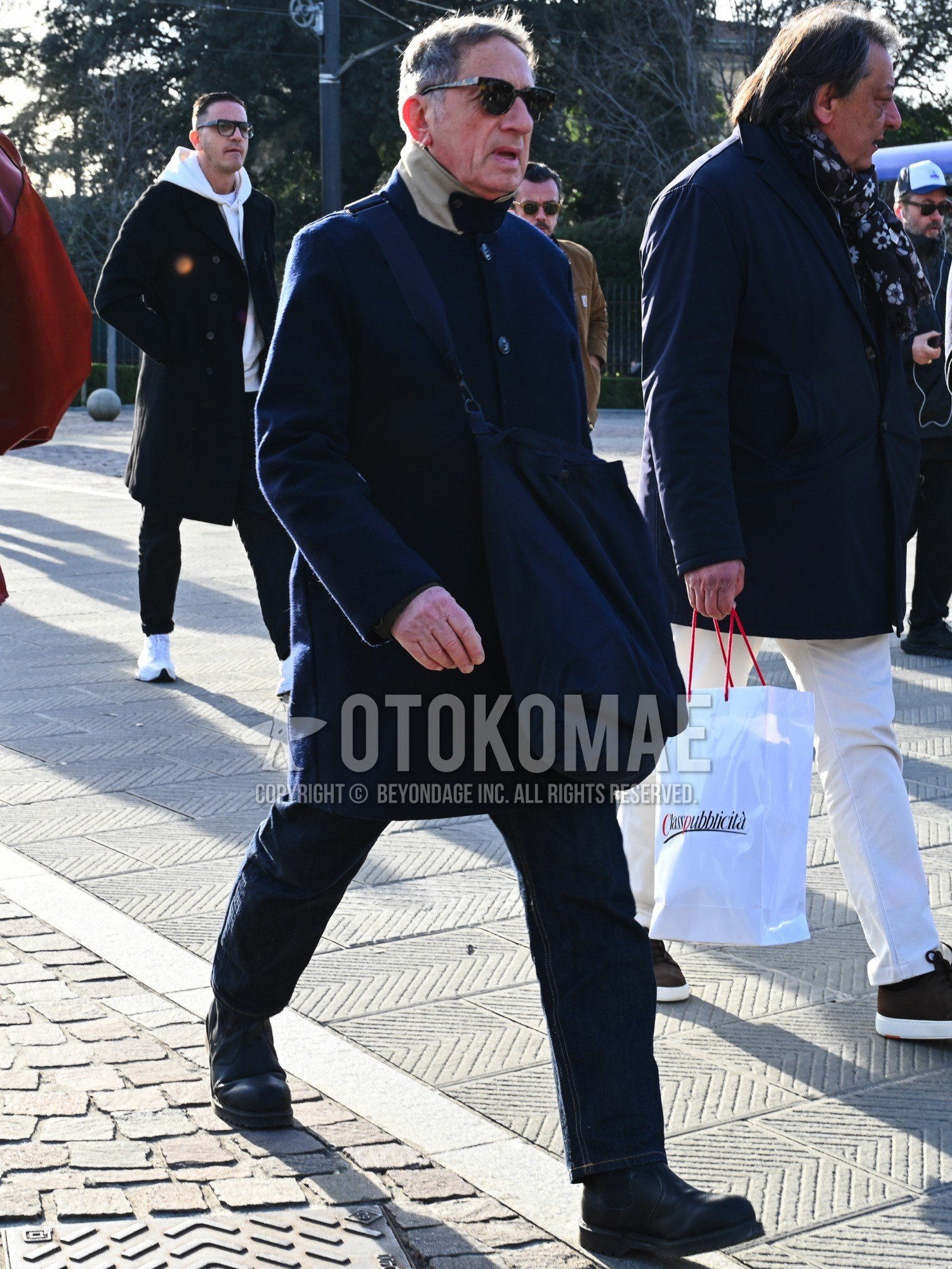 Men's autumn winter outfit with black plain sunglasses, navy plain stenkarrer coat, blue plain denim/jeans, black side-gore boots, navy plain shoulder bag.