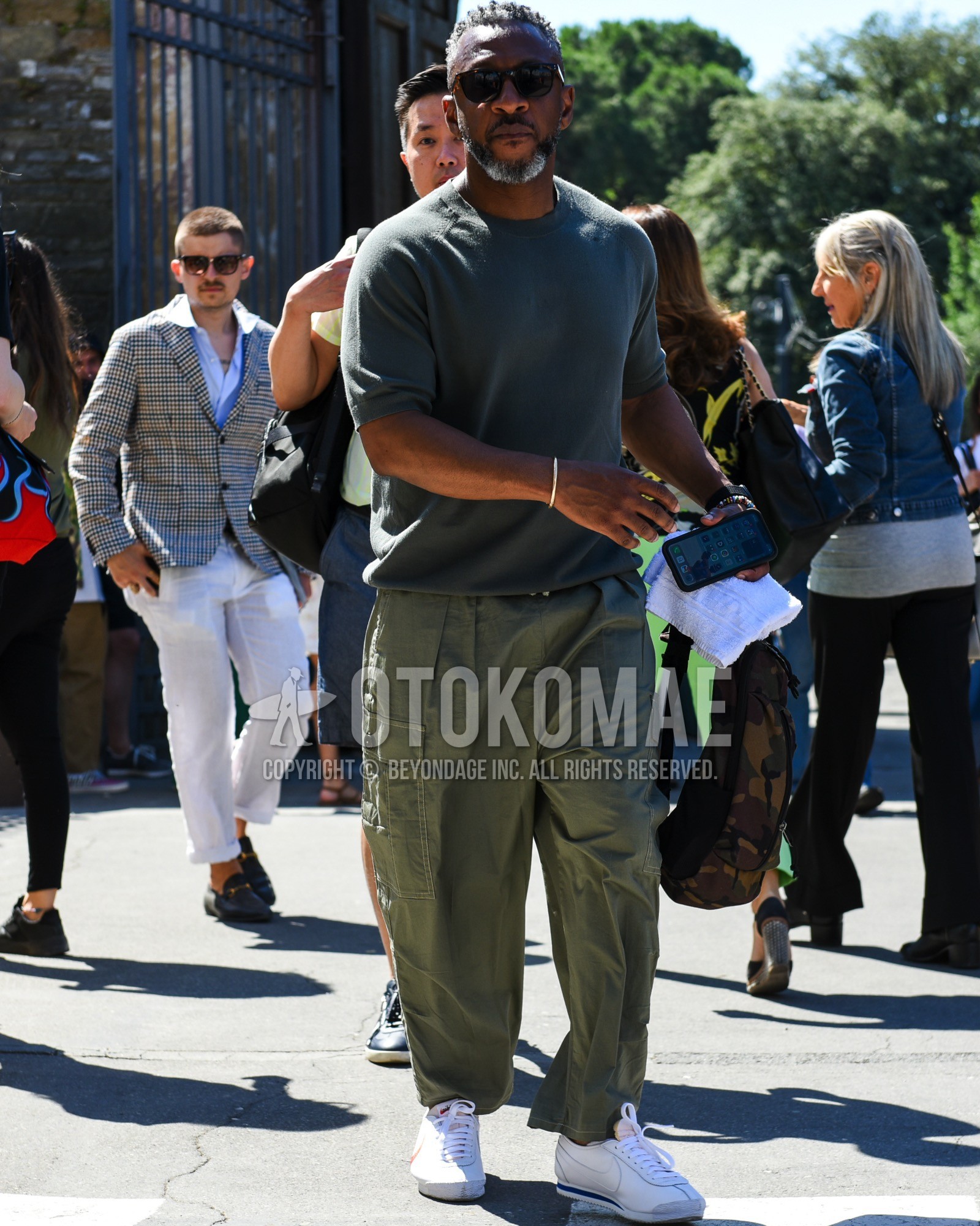 Men's spring summer outfit with brown plain sunglasses, gray plain t-shirt, olive green plain cargo pants, white low-cut sneakers, olive green camouflage body bag.