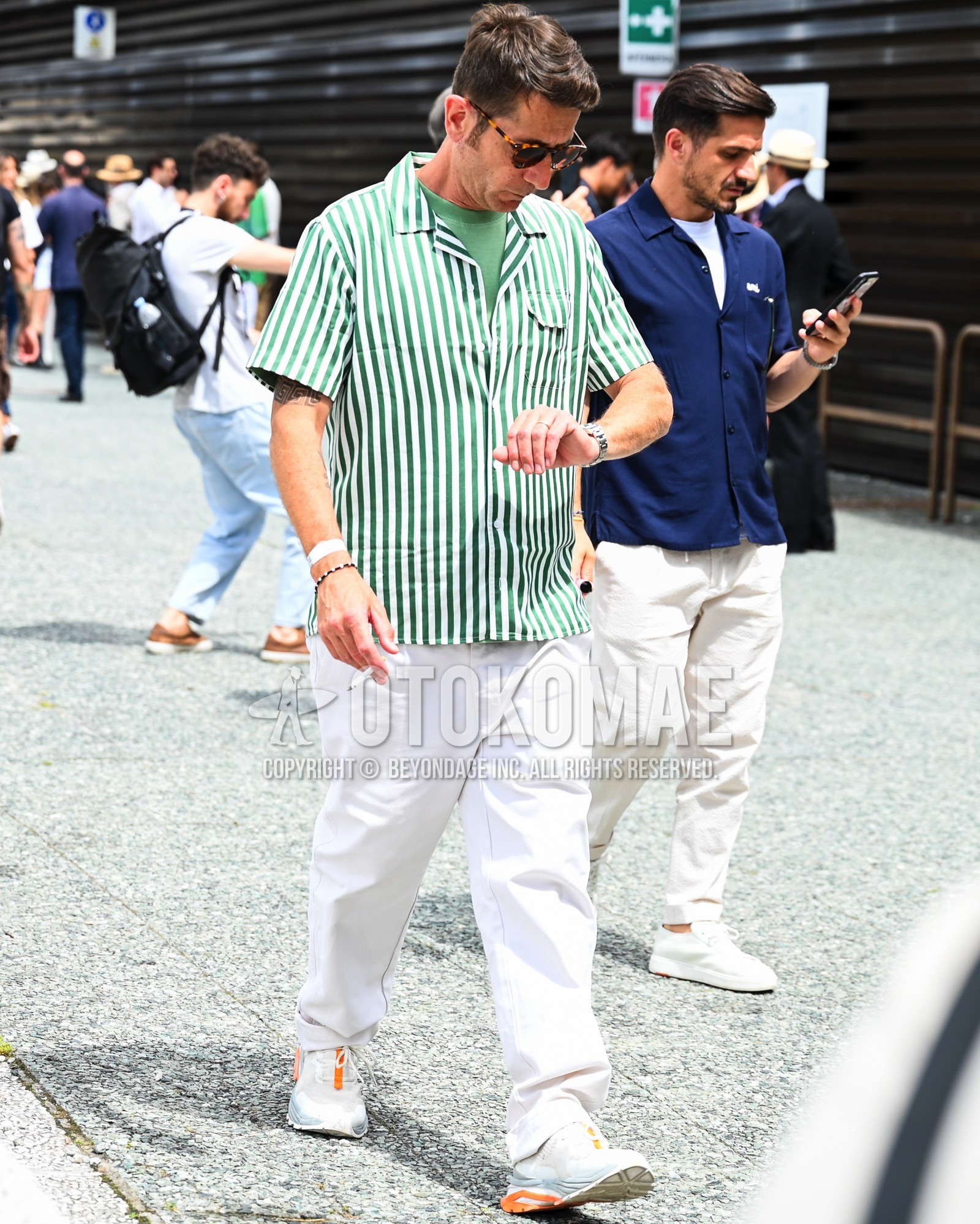 Men's spring summer outfit with green stripes shirt, green plain t-shirt, white plain chinos, white low-cut sneakers.