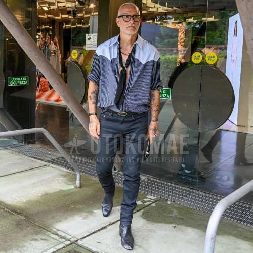 黒無地のメガネ、黒チェックのバンダナ/ネッカチーフ、マルチカラートップス/インナーのシャツ、黒無地のレザーベルト、黒無地のスキニーパンツ、黒のブーツを合わせた春夏のメンズコーデ・着こなし。