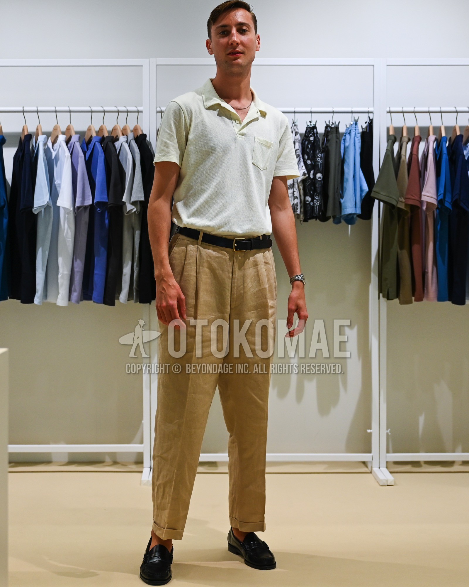 Men's spring summer outfit with white plain polo shirt, black plain leather belt, brown plain pleated pants, black coin loafers leather shoes.
