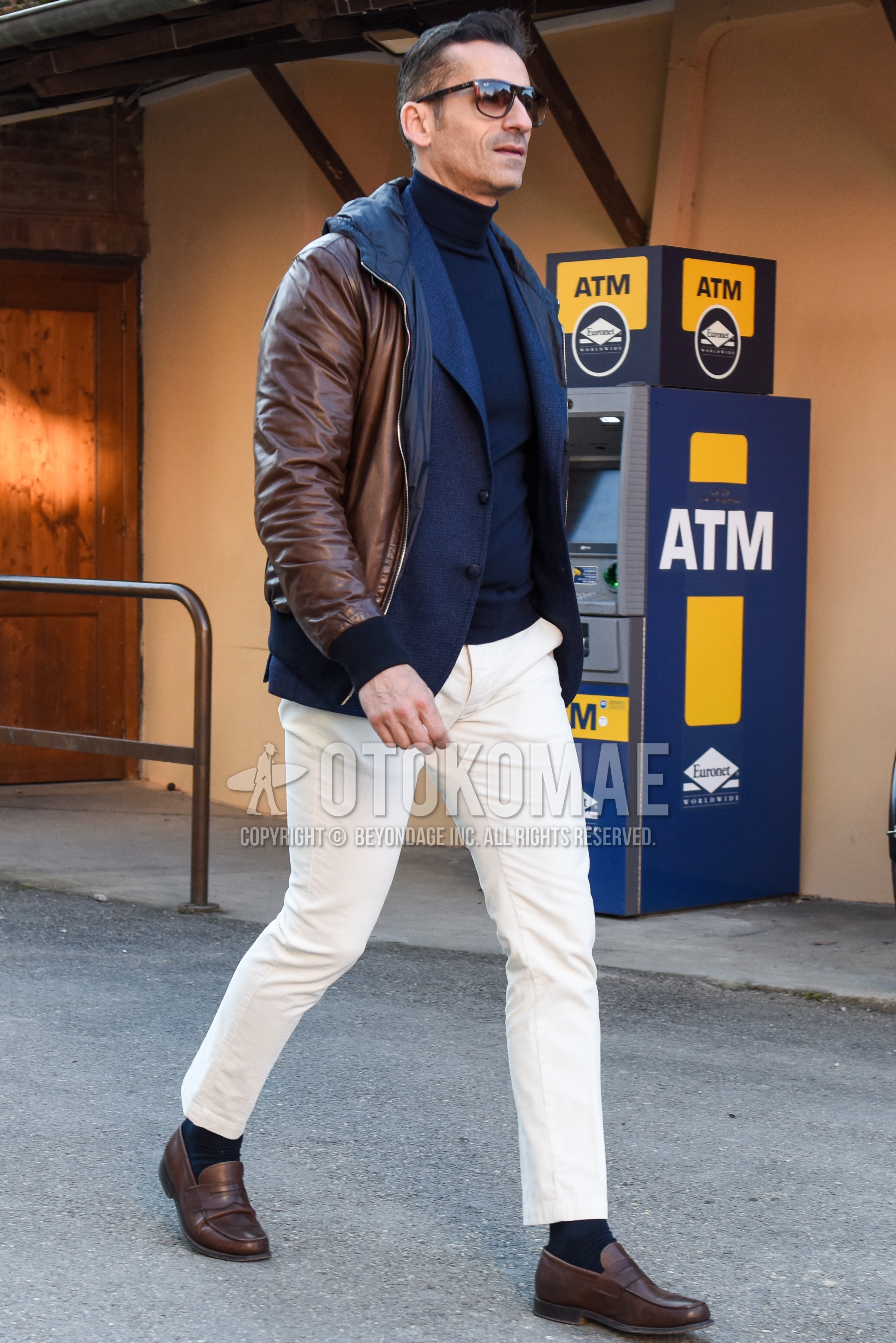 Men's autumn winter outfit with brown tortoiseshell sunglasses, brown plain leather jacket, gray plain tailored jacket, navy plain turtleneck knit, white plain chinos, white plain cropped pants, black plain socks, brown coin loafers leather shoes.
