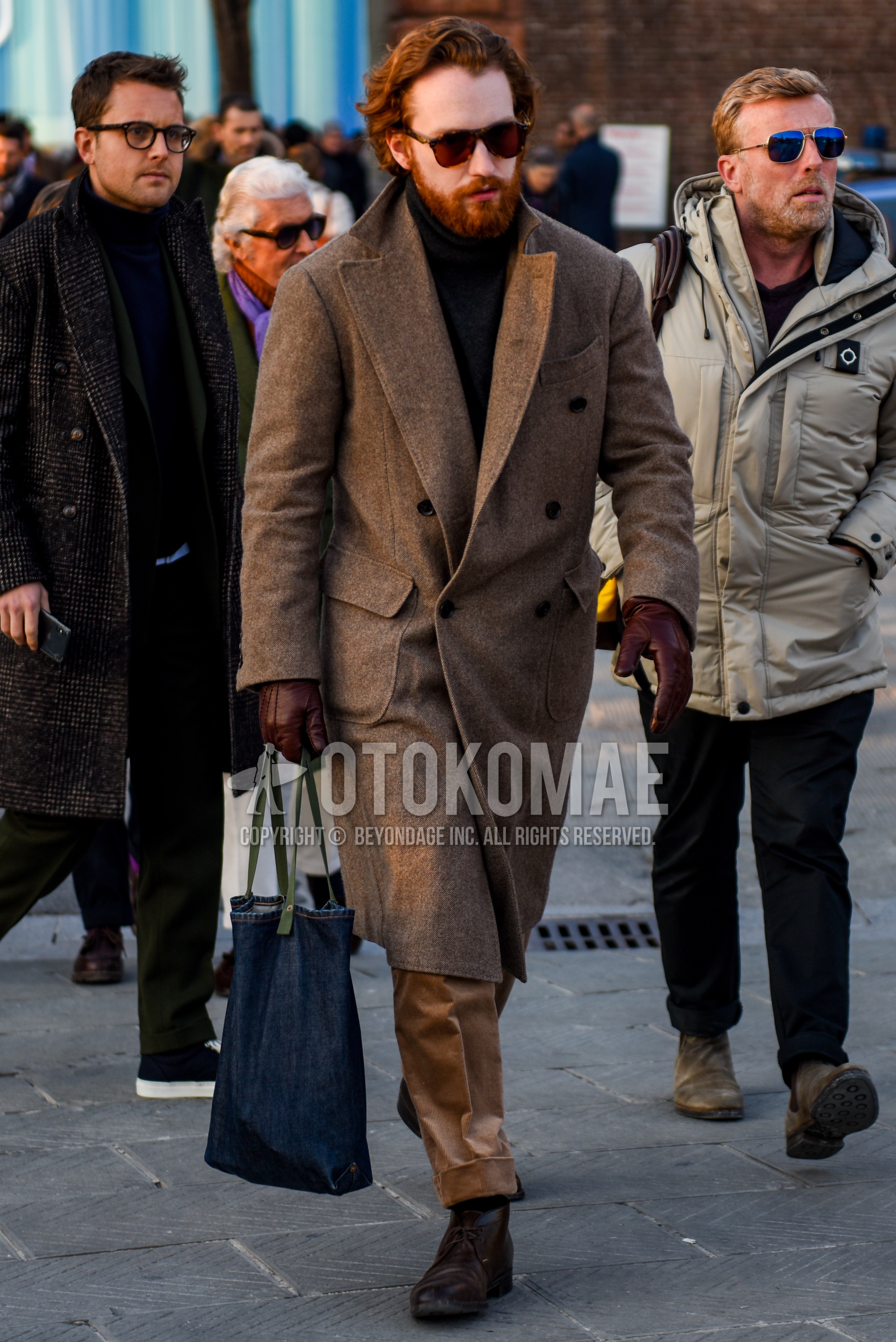 Men's autumn winter outfit with brown tortoiseshell sunglasses, beige plain chester coat, brown plain turtleneck knit, beige plain chinos, brown chukka boots, blue plain tote bag.