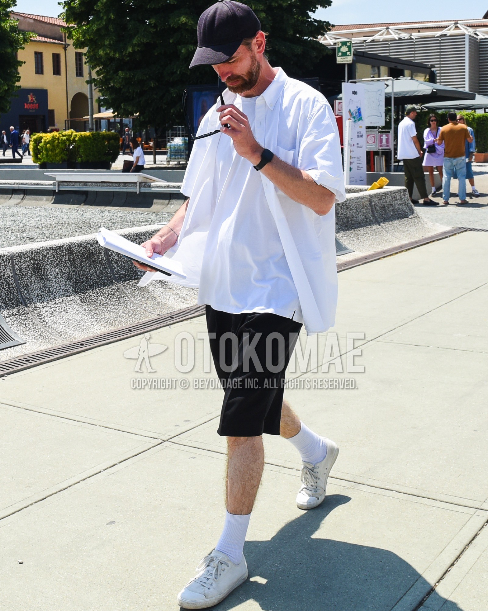 Men's spring summer outfit with navy plain baseball cap, white plain t-shirt, white plain shirt, black plain short pants, white plain socks, white sneakers.