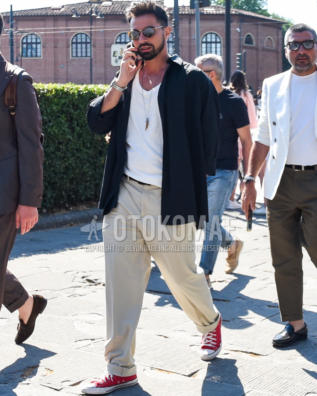Men's spring summer outfit with brown tortoiseshell sunglasses, white plain t-shirt, black plain shirt, black plain leather belt, beige plain slacks, red low-cut sneakers.