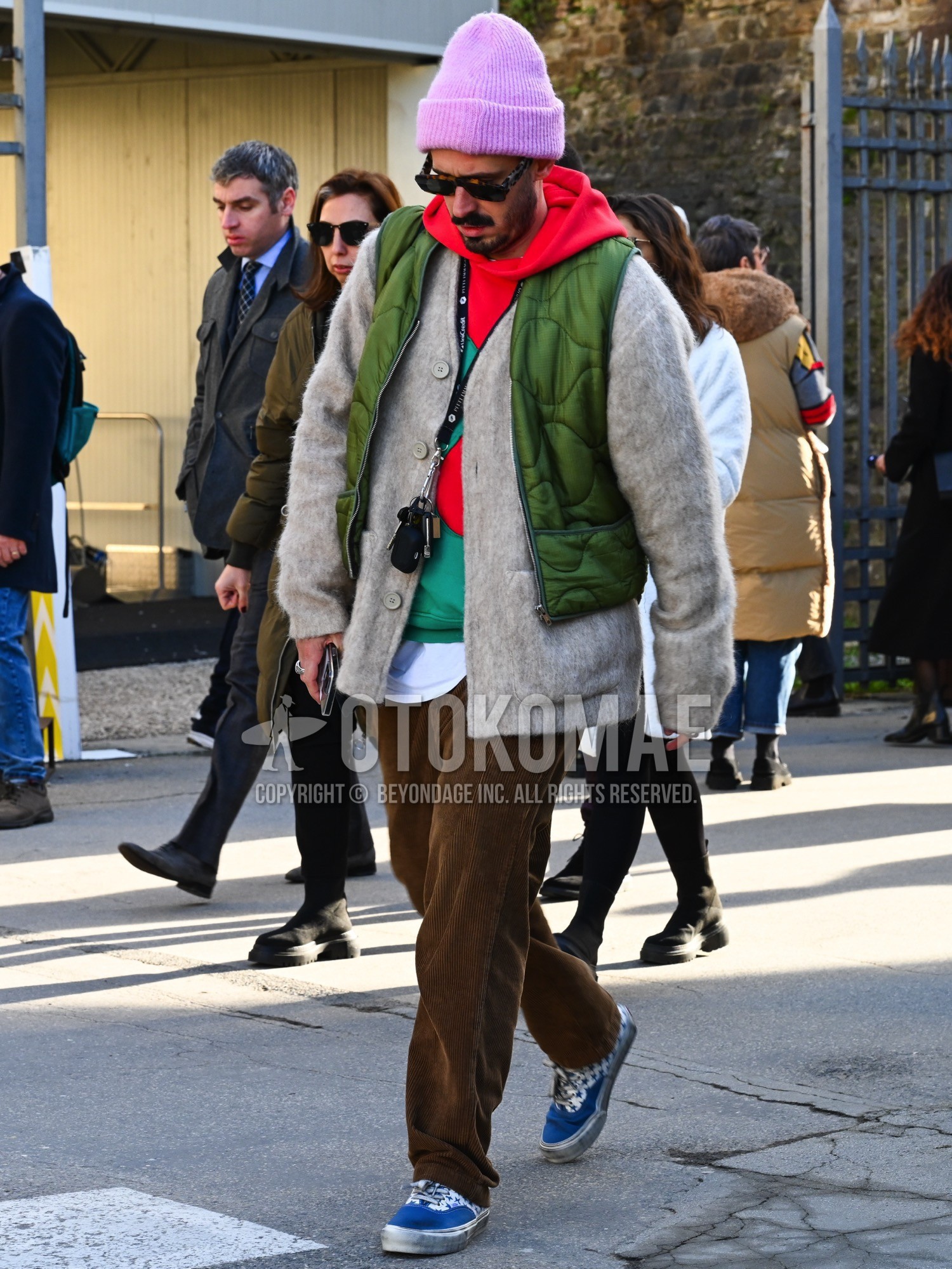 Men's autumn winter outfit with pink plain knit cap, brown tortoiseshell sunglasses, olive green plain quilted jacket, red plain hoodie, gray plain cardigan, brown plain winter pants (corduroy,velour), blue low-cut sneakers.