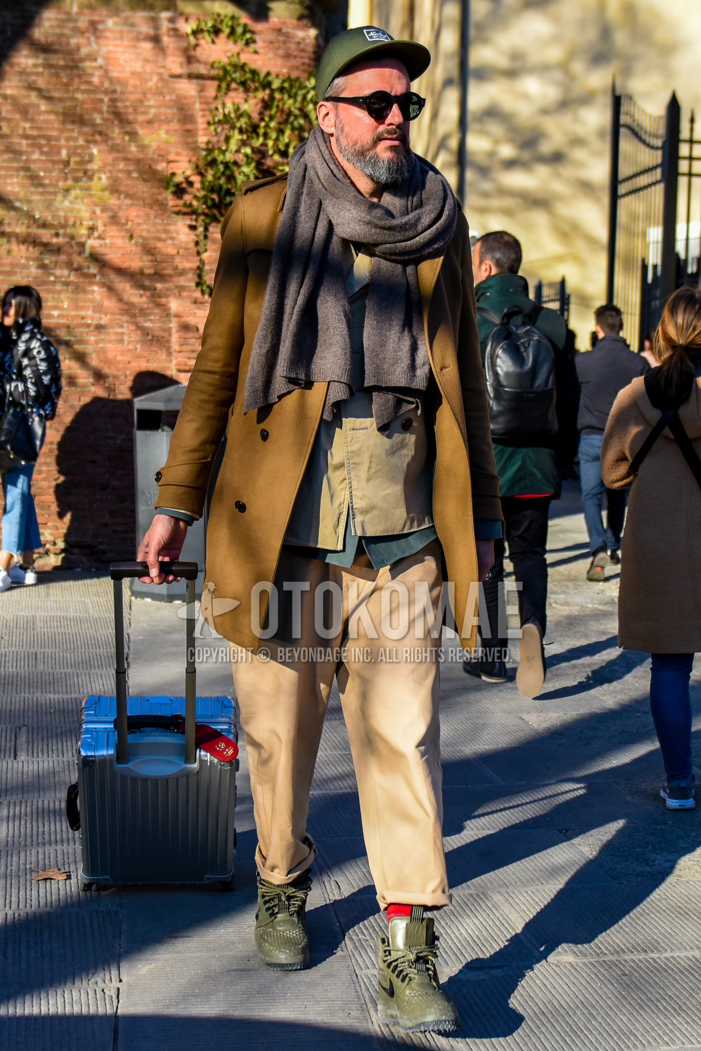 Men's winter outfit with olive green plain baseball cap, brown plain scarf, brown plain p coat, beige plain chinos, olive green high-cut sneakers.