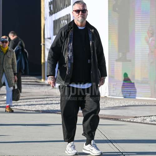 レッド無地のサングラス、バブアーのダークグレー無地のアウター、カーハートの黒無地のトレーナー、黒無地のワイドパンツ、ナイキの白ローカットのスニーカーを合わせた秋冬のメンズコーデ・着こなし。