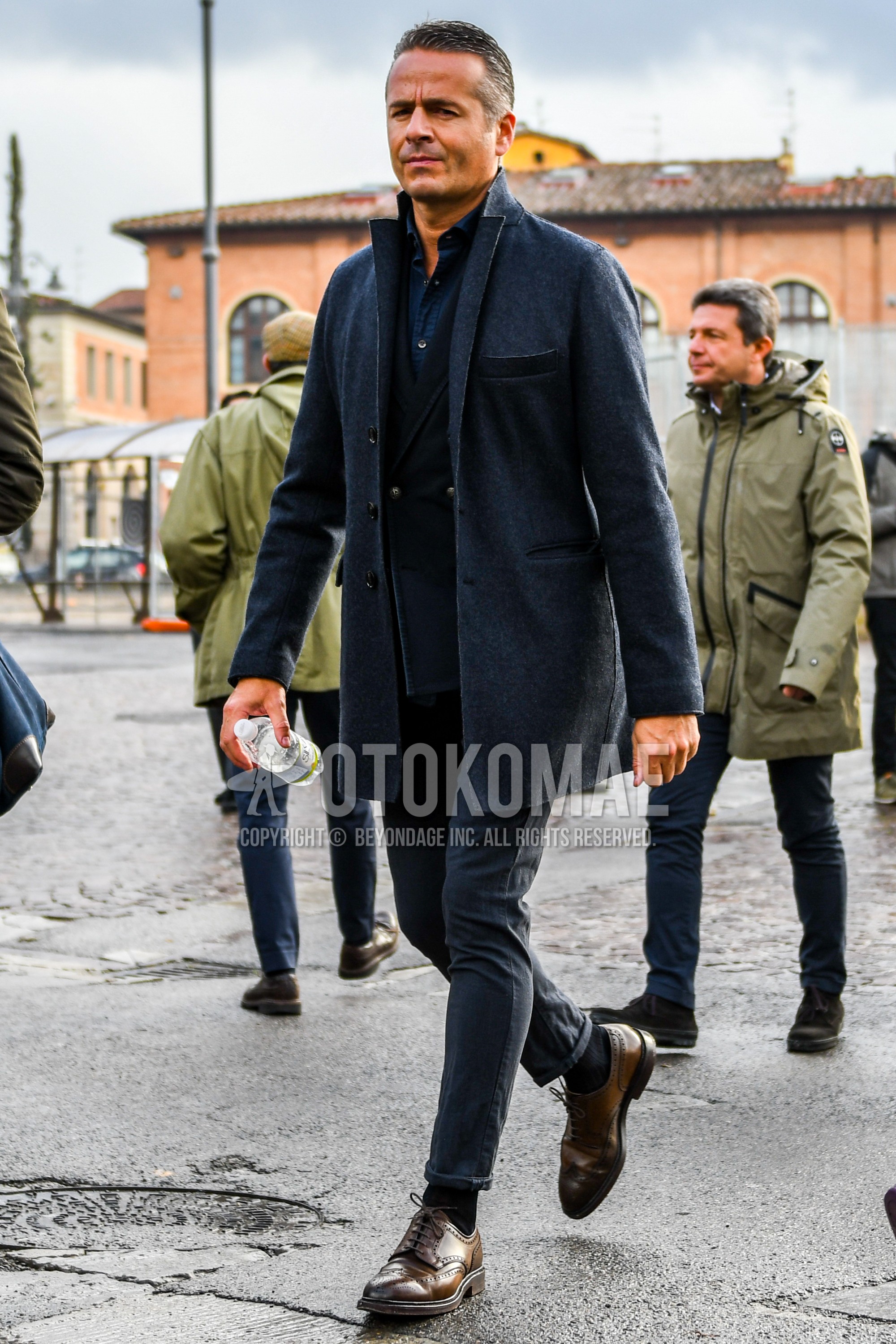 Men's winter outfit with dark gray plain chester coat, black plain tailored jacket, navy plain shirt, dark gray plain cotton pants, black plain socks, brown brogue shoes leather shoes.