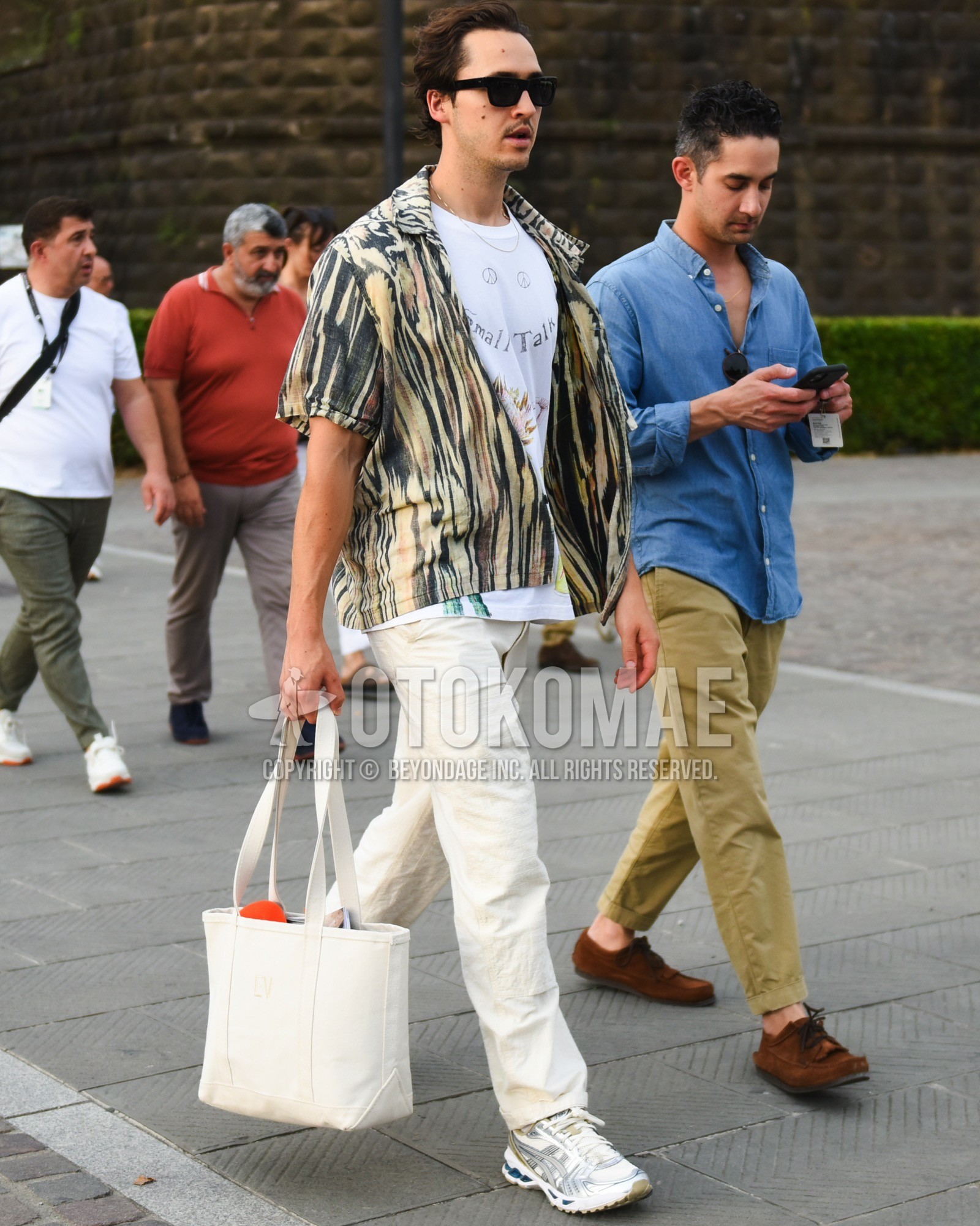 Men's spring summer outfit with black plain sunglasses, yellow black zebra shirt, white graphic t-shirt, white plain cotton pants, white gray low-cut sneakers, white plain tote bag.