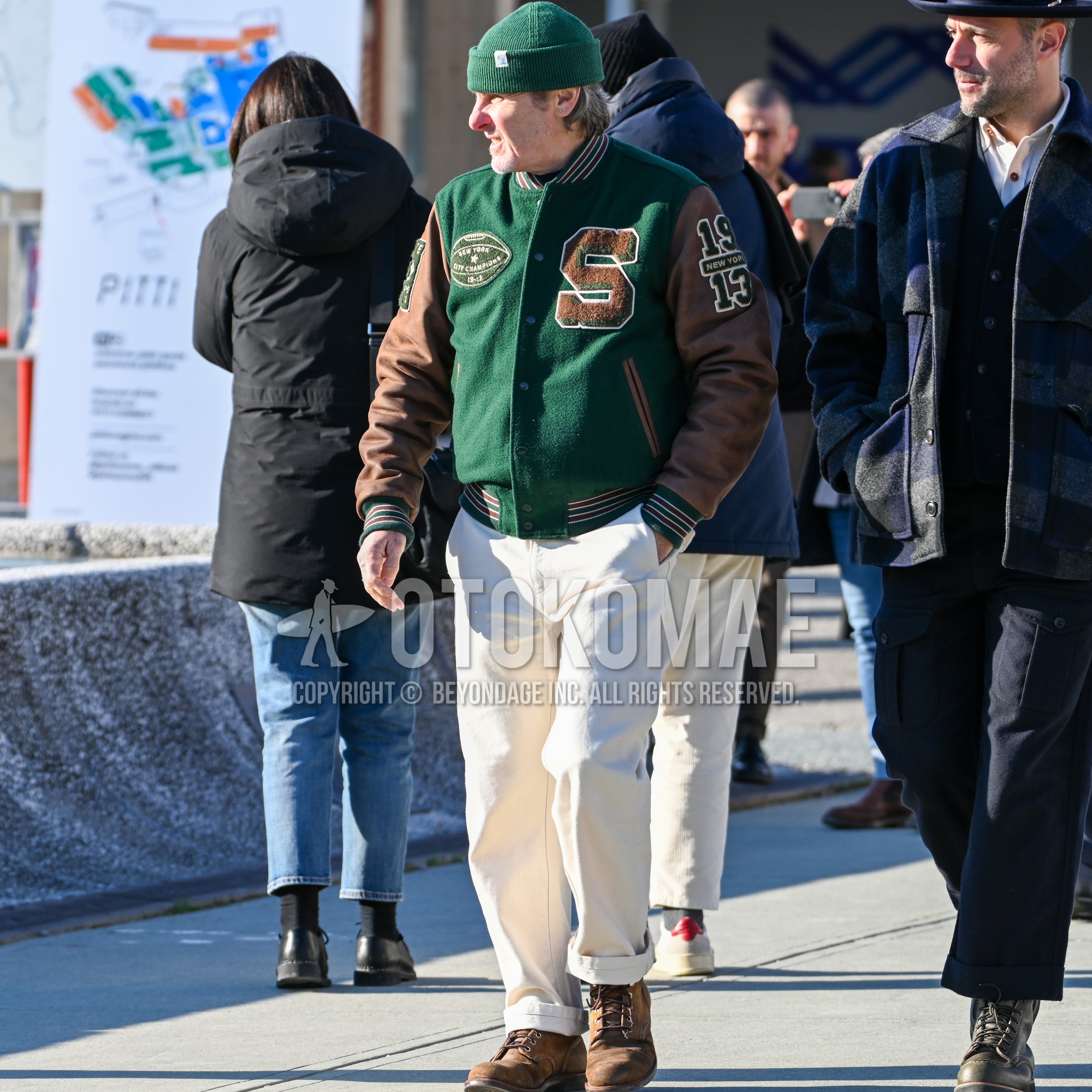Men's autumn winter outfit with green one point knit cap, green brown deca logo stadium jacket, white plain cotton pants, brown work boots.