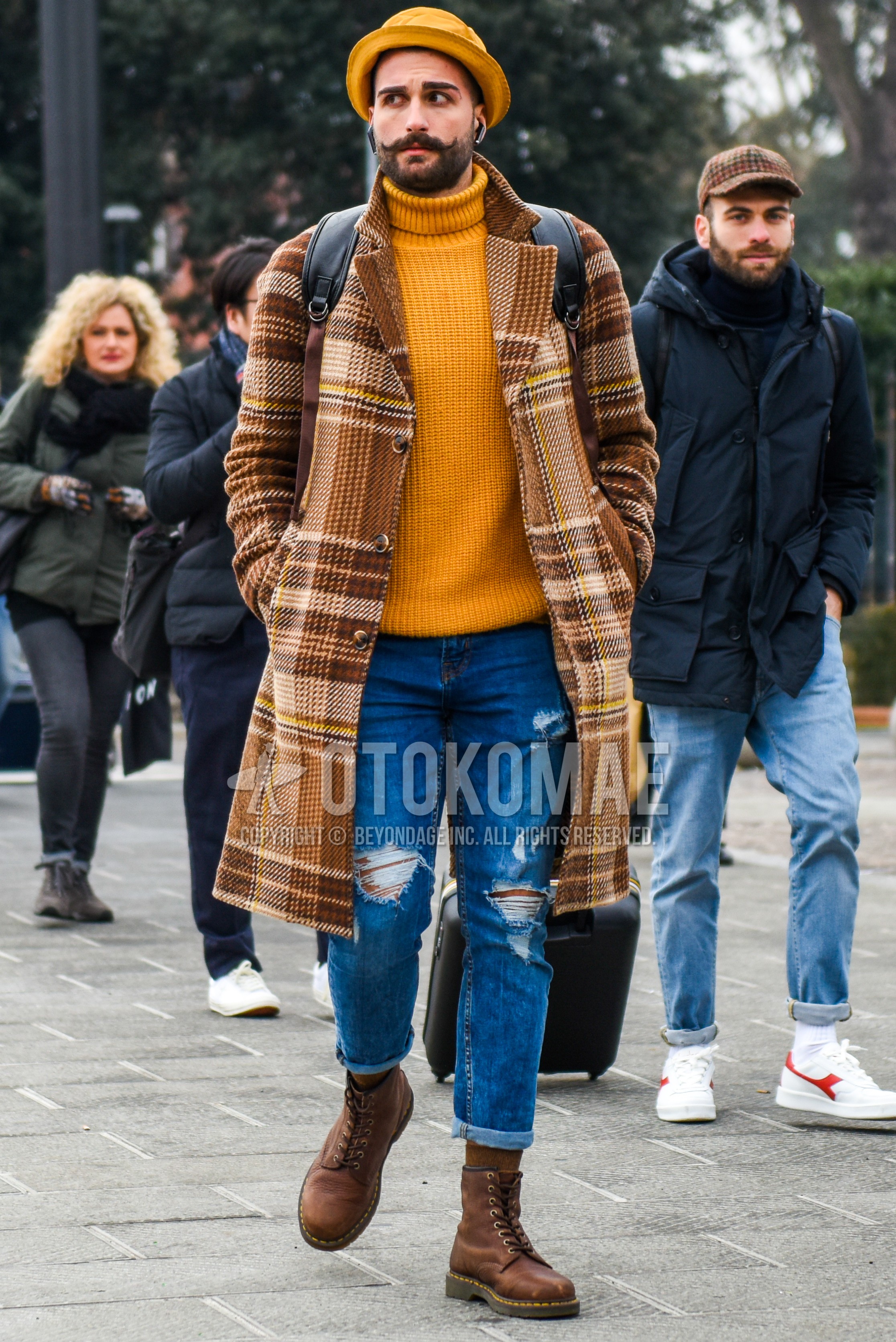 Men's autumn winter outfit with yellow plain hat, brown check ulster coat, beige plain turtleneck knit, blue plain damaged jeans, brown plain socks, brown work boots.