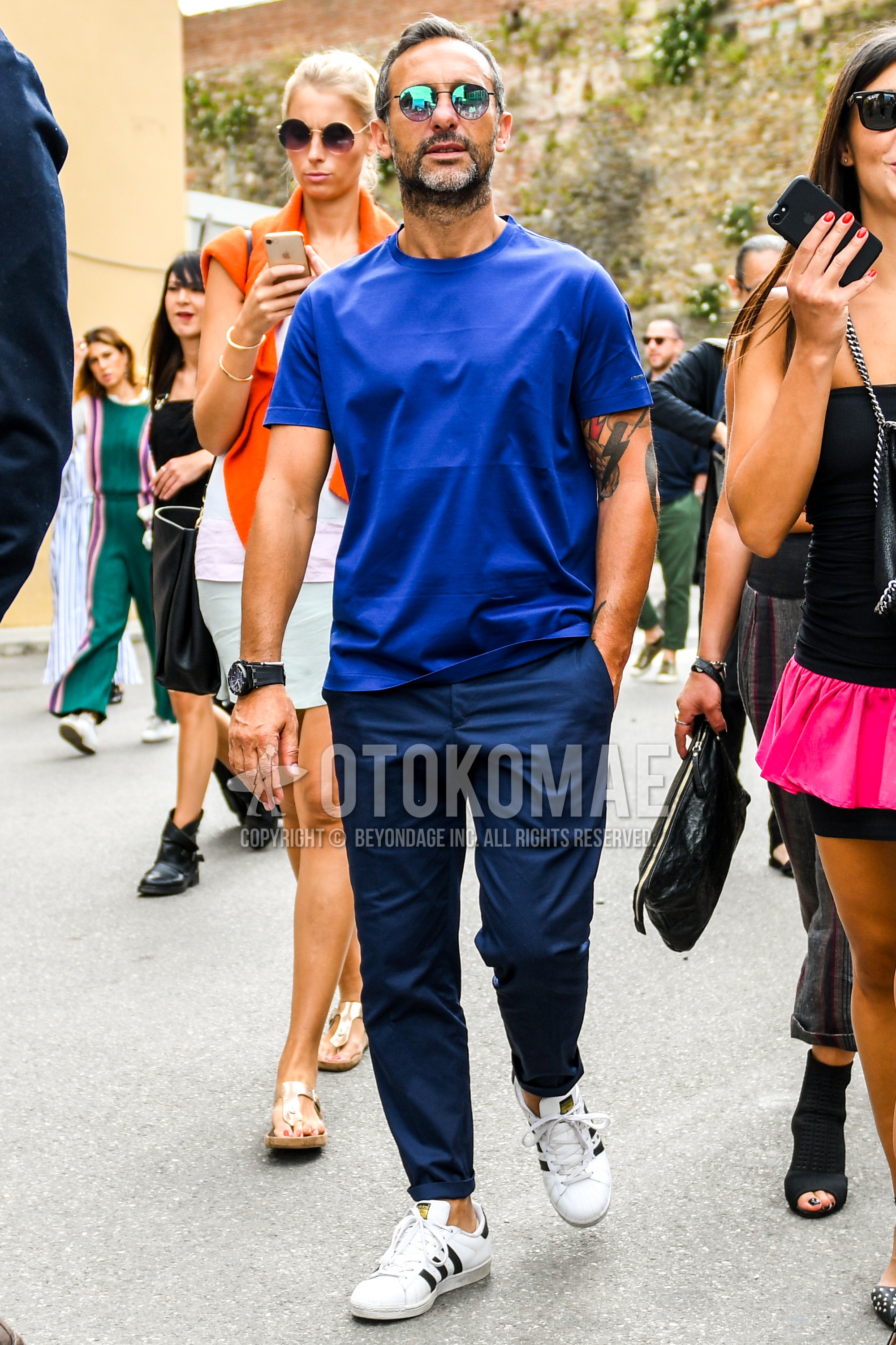 Men's summer outfit with plain sunglasses, blue plain t-shirt, navy plain chinos, white low-cut sneakers.