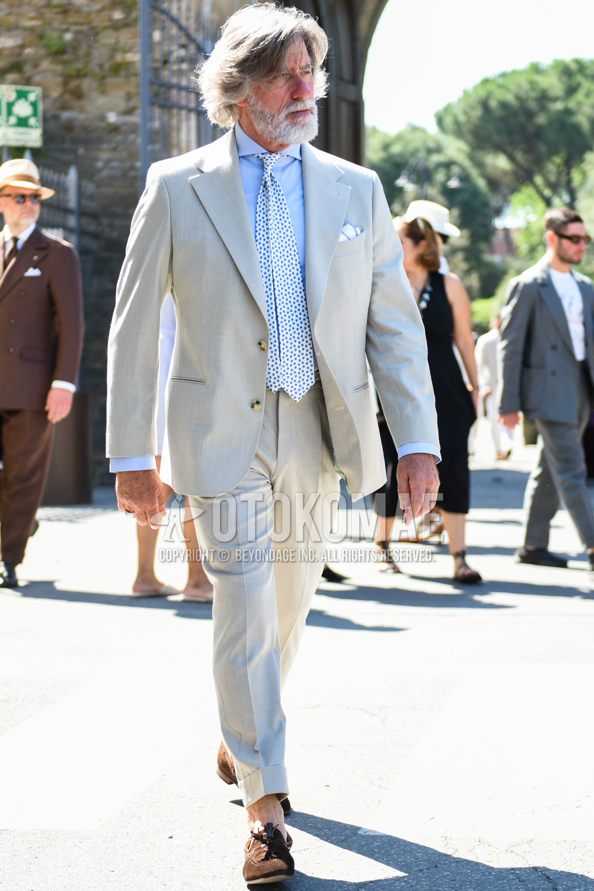 Men's spring summer outfit with light blue plain shirt, brown tassel loafers leather shoes, beige gray plain suit, white light blue dots necktie.