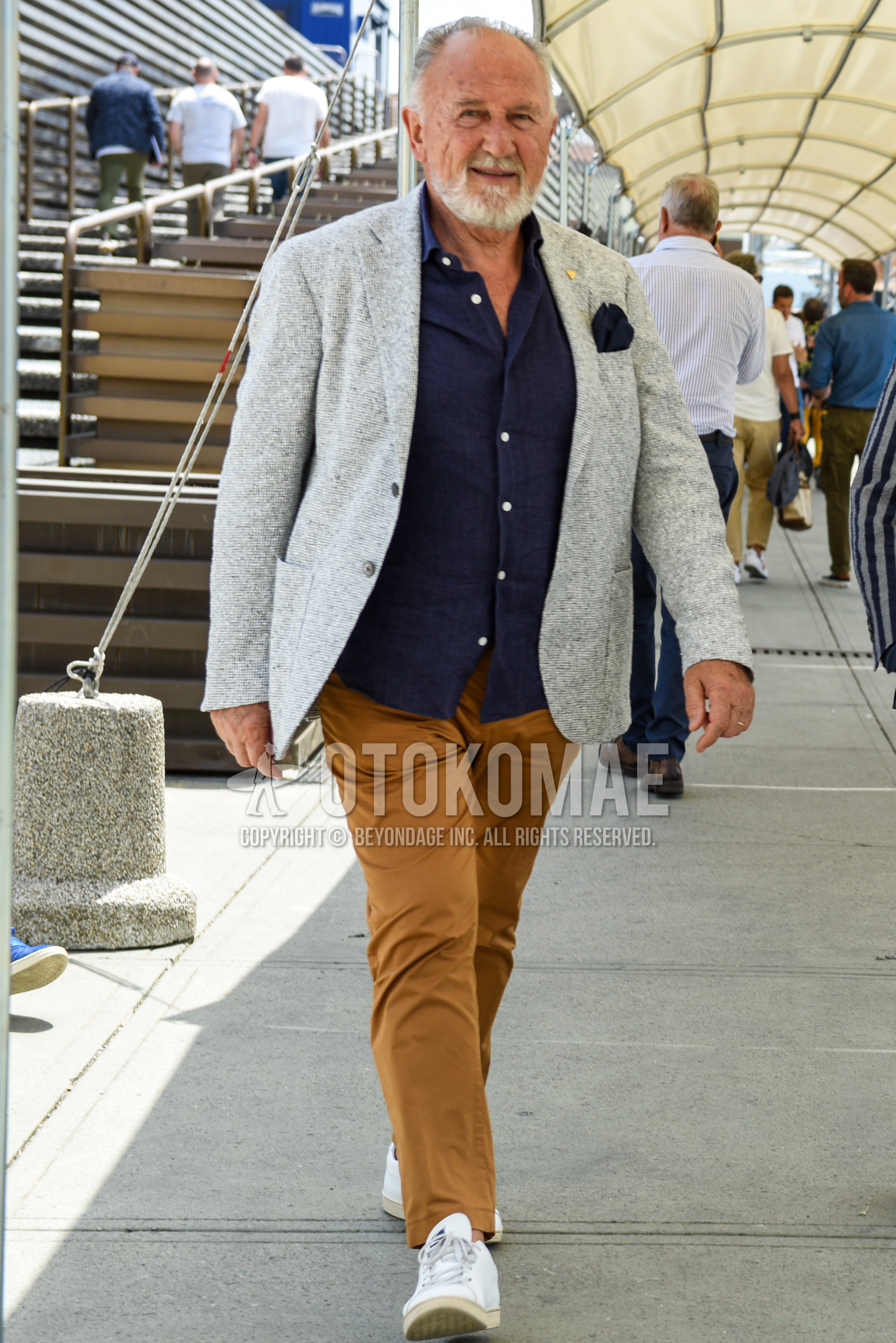 Men's spring summer autumn outfit with gray plain tailored jacket, navy plain shirt, beige plain chinos, white low-cut sneakers.