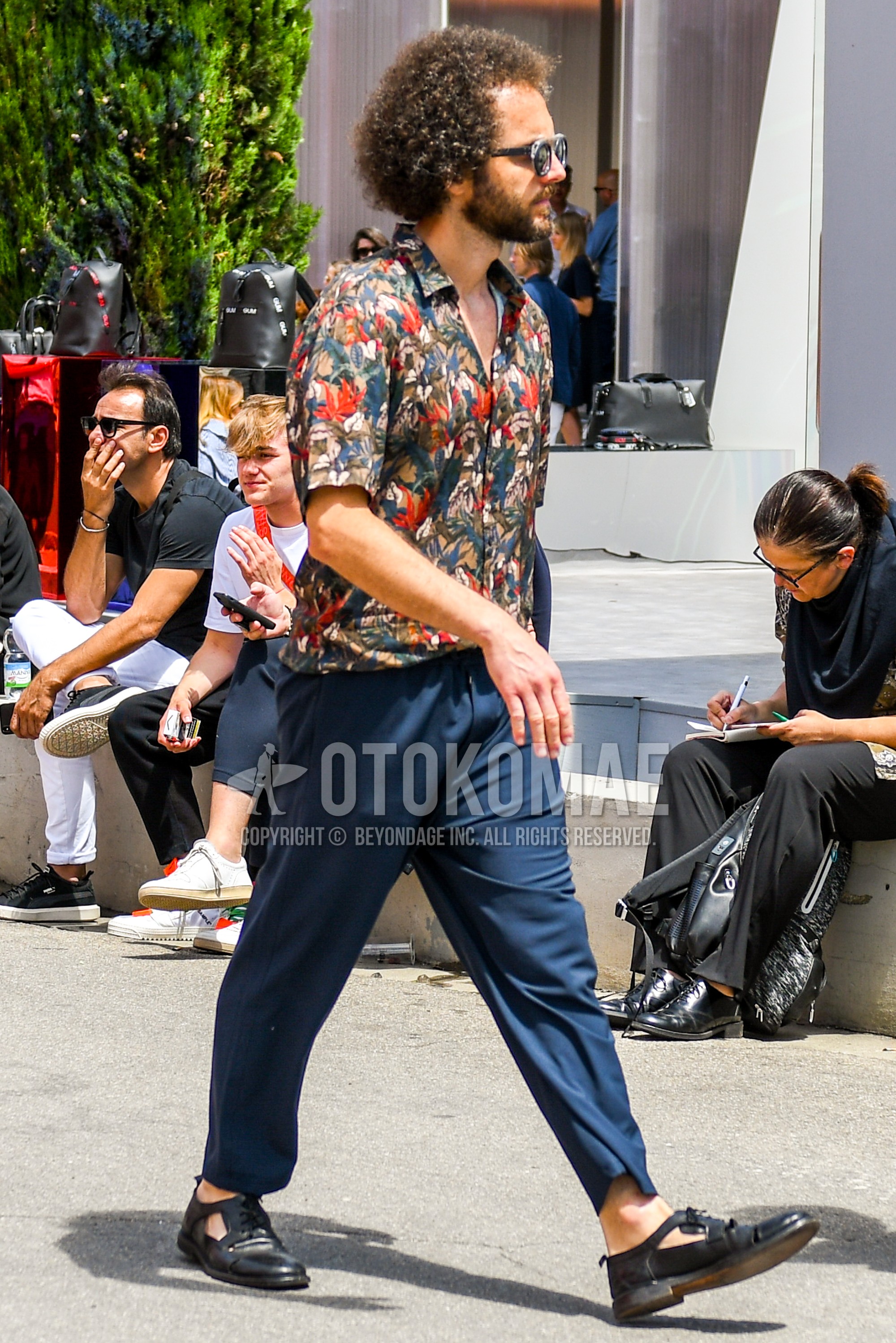 Men's summer outfit with plain sunglasses, botanical shirt, navy plain ankle pants, black leather sandals.