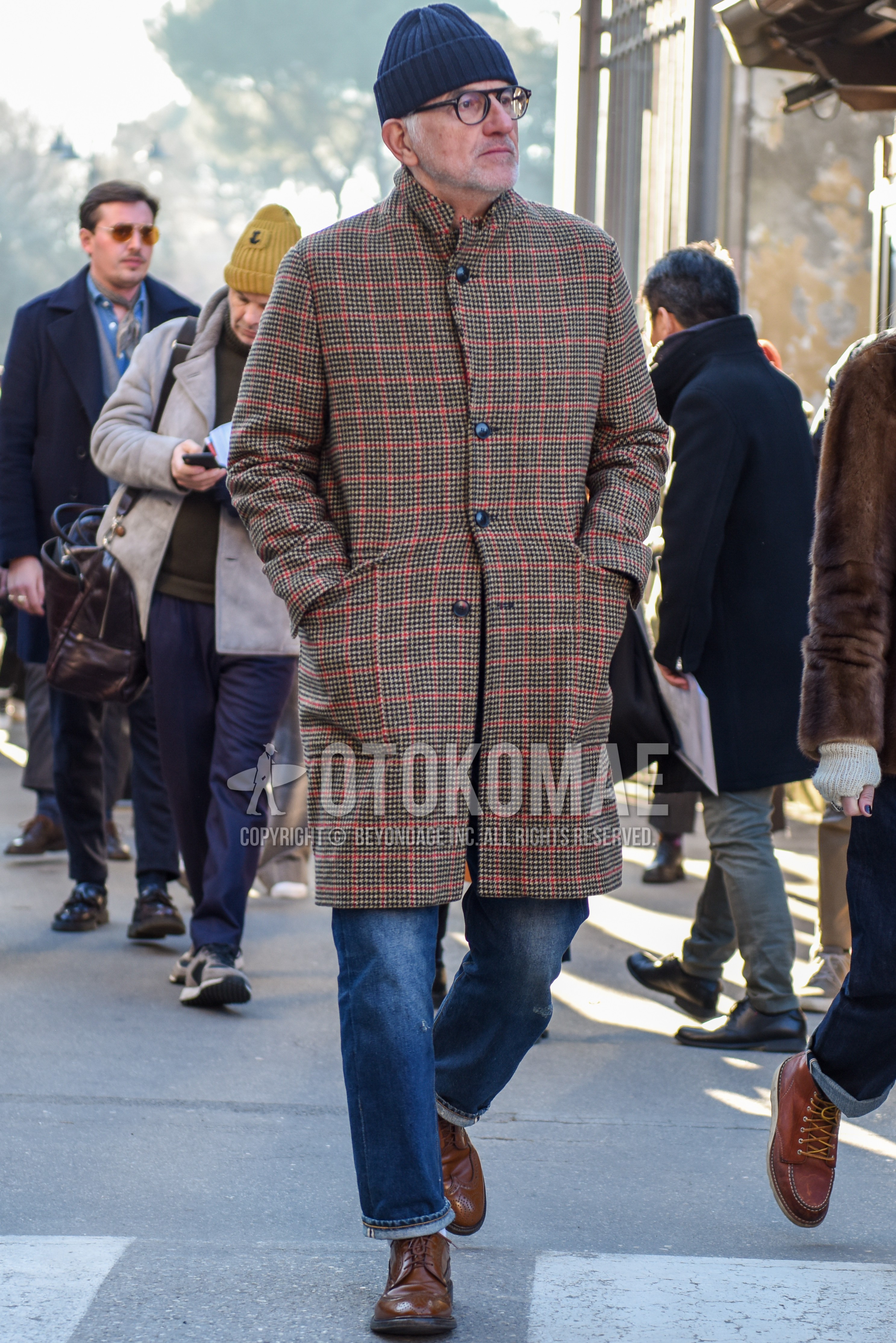 Men's autumn winter outfit with gray plain knit cap, black plain glasses, brown check stenkarrer coat, blue plain denim/jeans, brown wing-tip shoes leather shoes.
