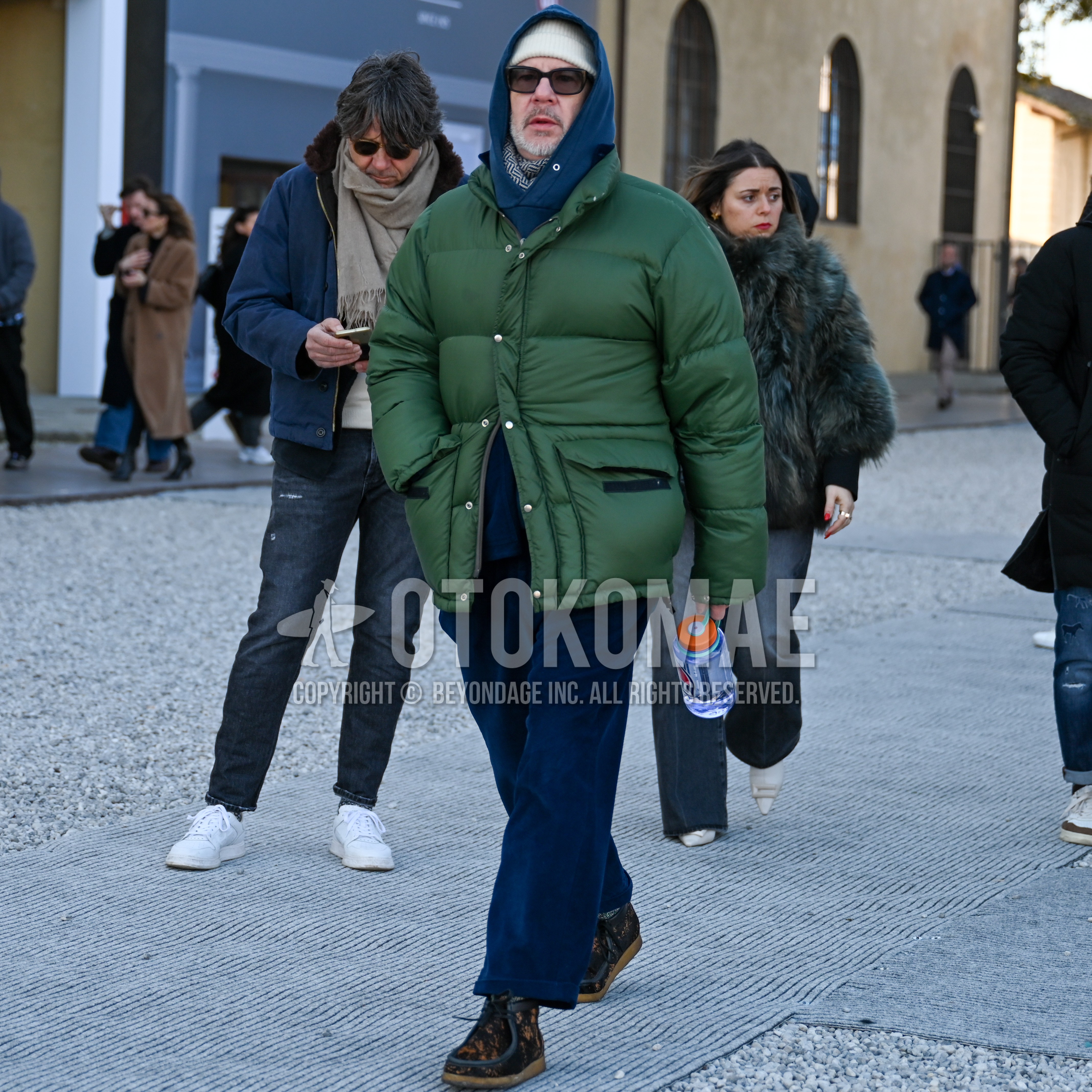 Men's winter outfit with white plain knit cap, brown plain sunglasses, olive green plain down jacket, blue plain hoodie, blue plain winter pants (corduroy,velour), brown  boots.