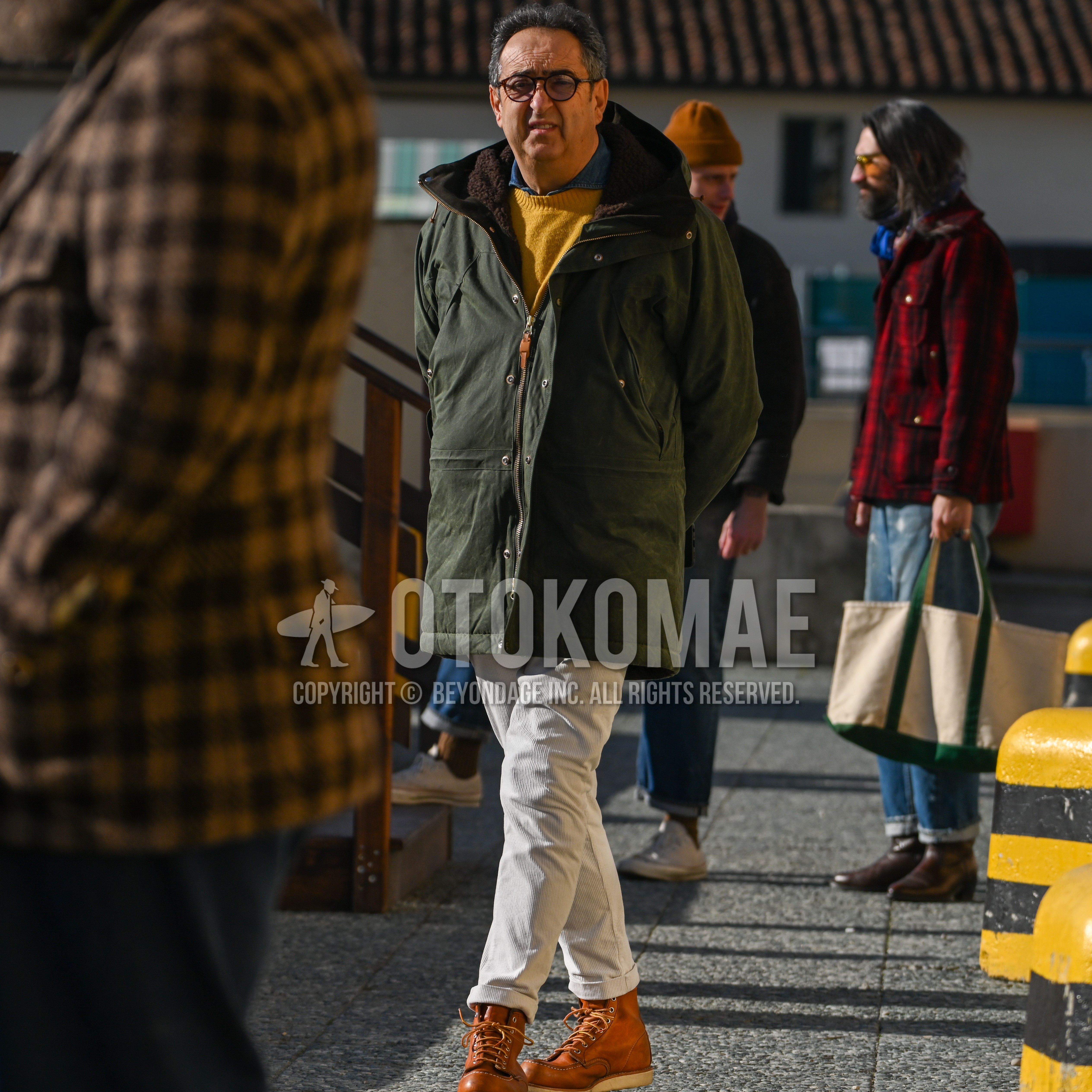 Men's autumn winter outfit with brown plain glasses, olive green outerwear hooded coat, plain denim shirt/chambray shirt, yellow plain sweater, beige plain winter pants (corduroy,velour), brown work boots.