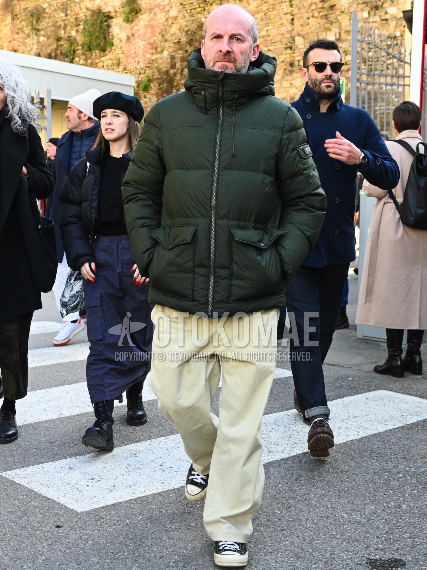 Men's autumn winter outfit with olive green plain down jacket, beige plain chinos, black low-cut sneakers.